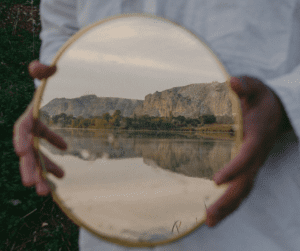 a person holds up a reflection in a mirror of mountains