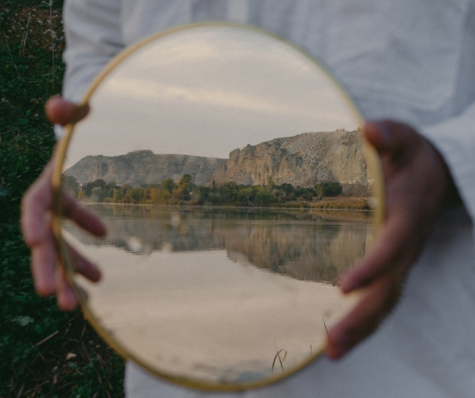 a person holds up a reflection in a mirror of mountains