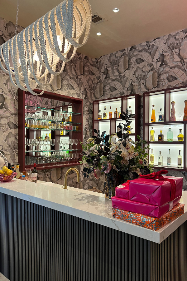 an interior design brand vignette of a bar with pink wrapped gifts, a funky light, and palm wallpaper