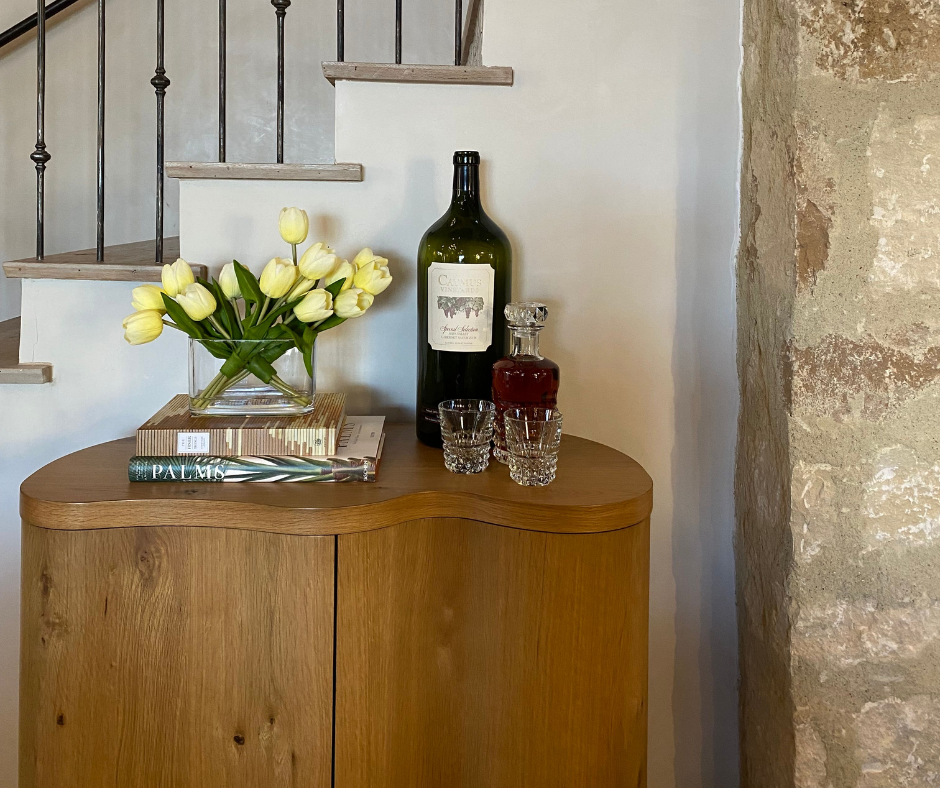 a sideboard with books, tulips, a bottle of alcohol, decanter, and two glasses
