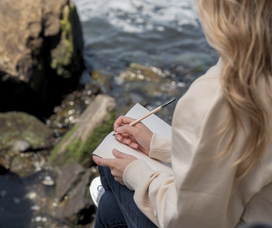 woman at the beach answering manifestation journal prompts