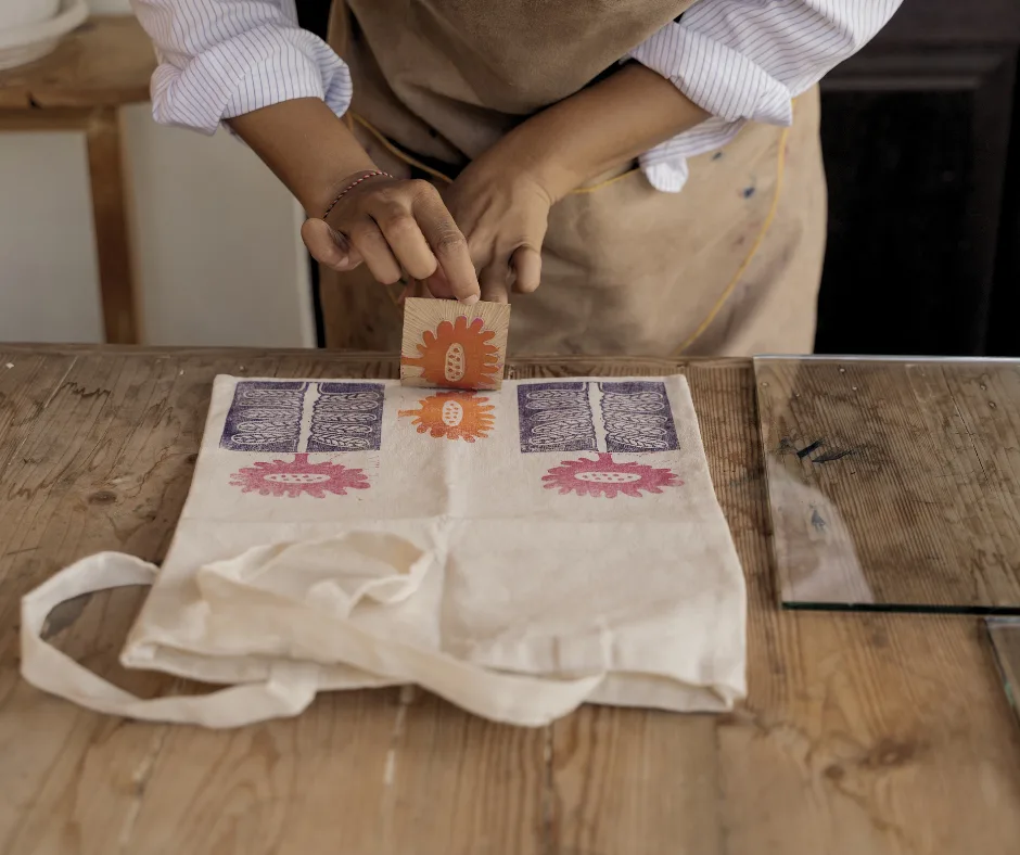 woman printing flower designs on a tote bag in preparation for art fairs and craft shows