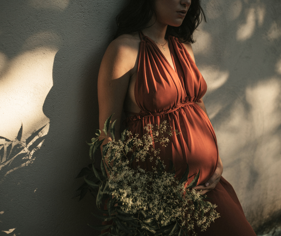 pregnant woman wearing an orange dress with flowers and shadows over her as the featured image for our article about fertility tracking devices