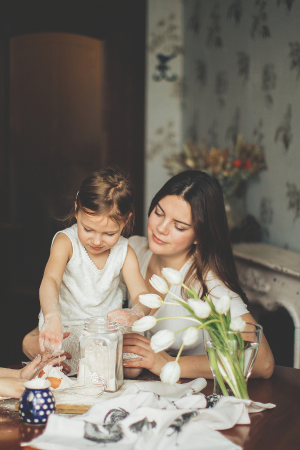 a mother with her child in the kitchen baking in front of a vase of tulips