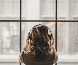 the back of a woman's head as she looks out the window wearing headphones to use her language learning app