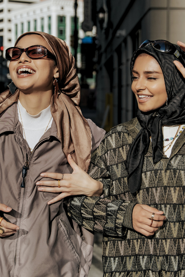 two female friends wearing head scarves while walking down the street and laughing