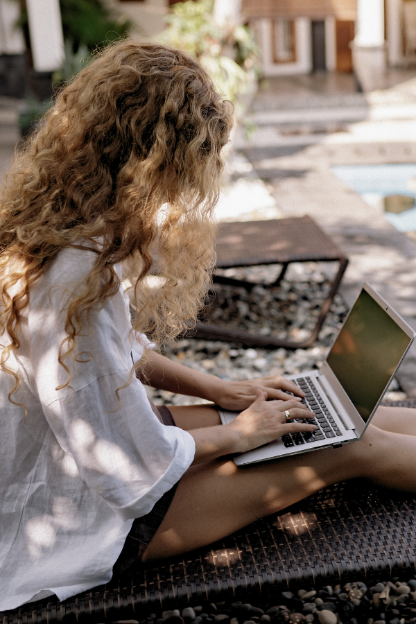 a woman with curly hair works by the pool on her laptop