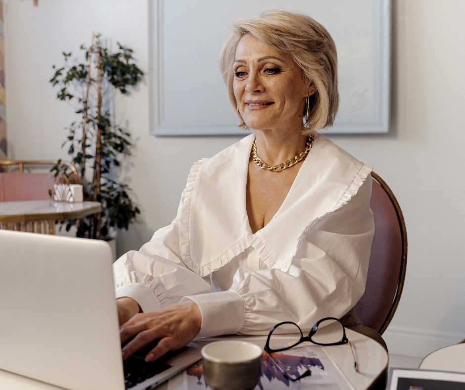 older woman in a white blouse on her computer