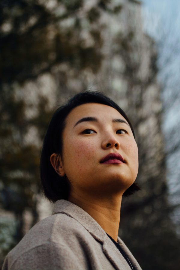 a woman stands in front of trees wearing a gray blazer