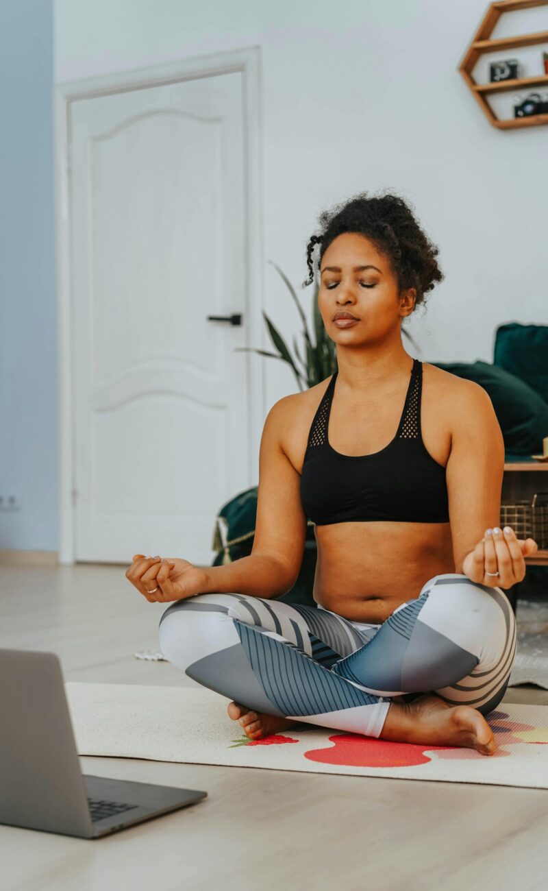 A woman sitting in lotus pose, meditating in front of her laptop