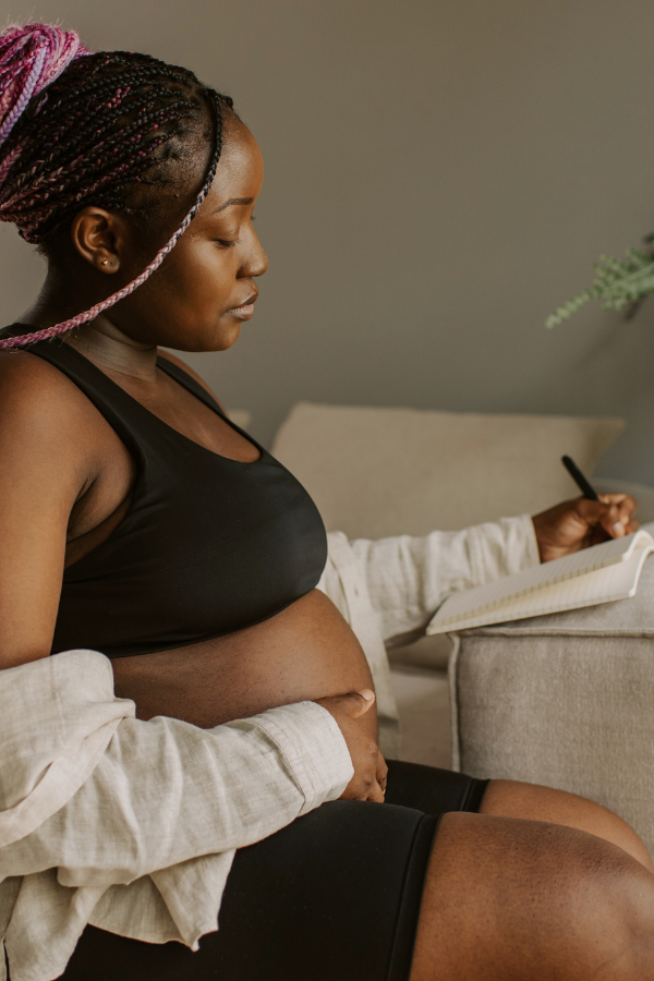 a pregnant woman journals while sitting on her couch