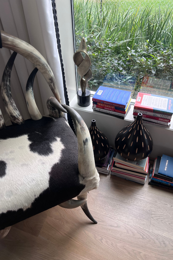 a black and white room with a natural chair, books, vases, and other elements with an off white wall color