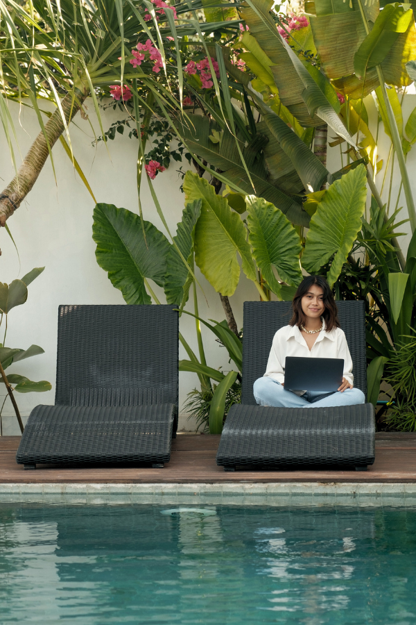 woman sitting on a lounge chair with her laptop by the pool