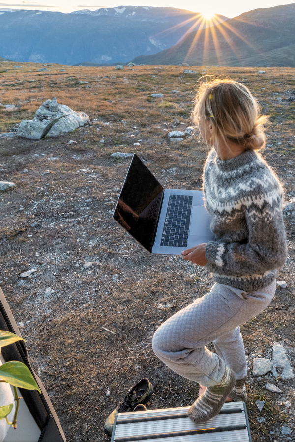 a woman stands outside a trailer holding a laptop