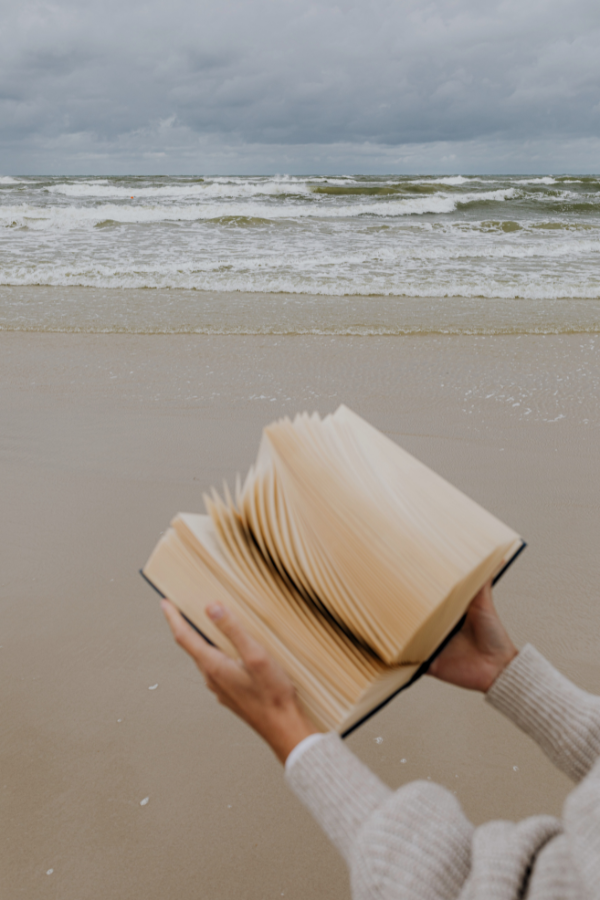 a woman holding up a book in front of the ocean