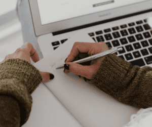 a woman writing in front of a laptop