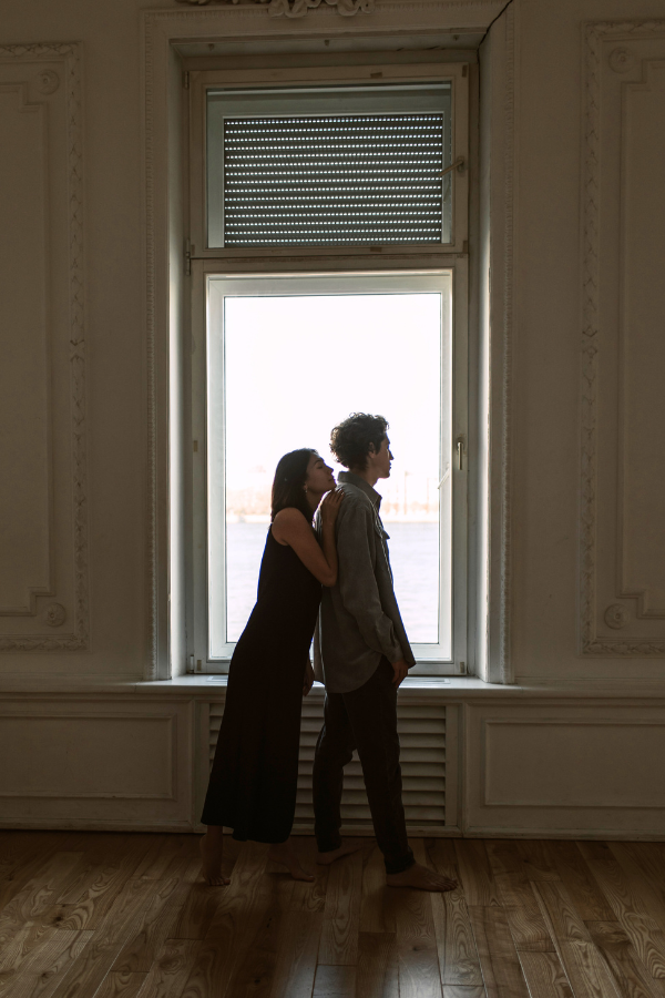 a couple embraces in front of a window