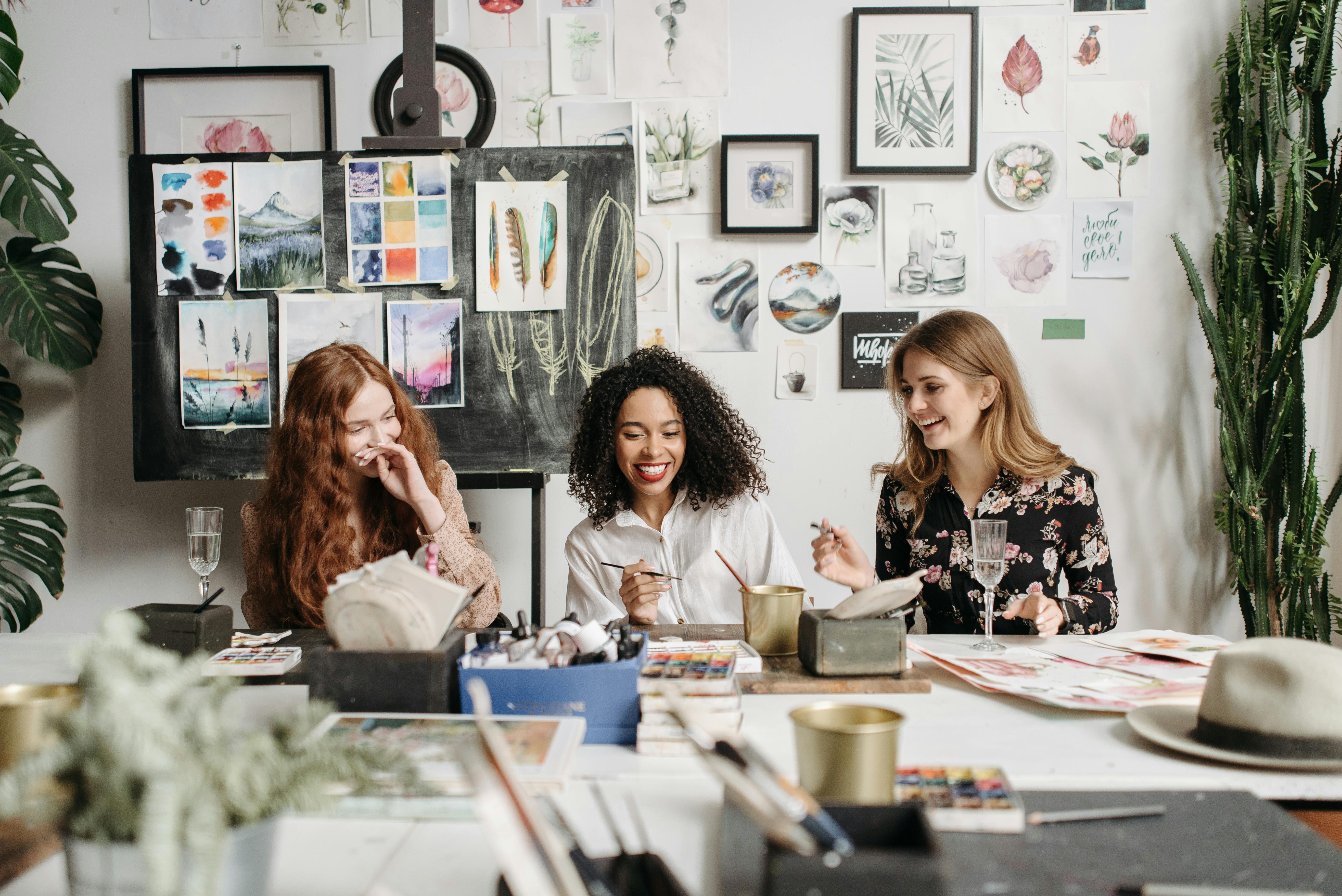 Three women engaged in an art session, surrounded by colorful paintings and art supplies.