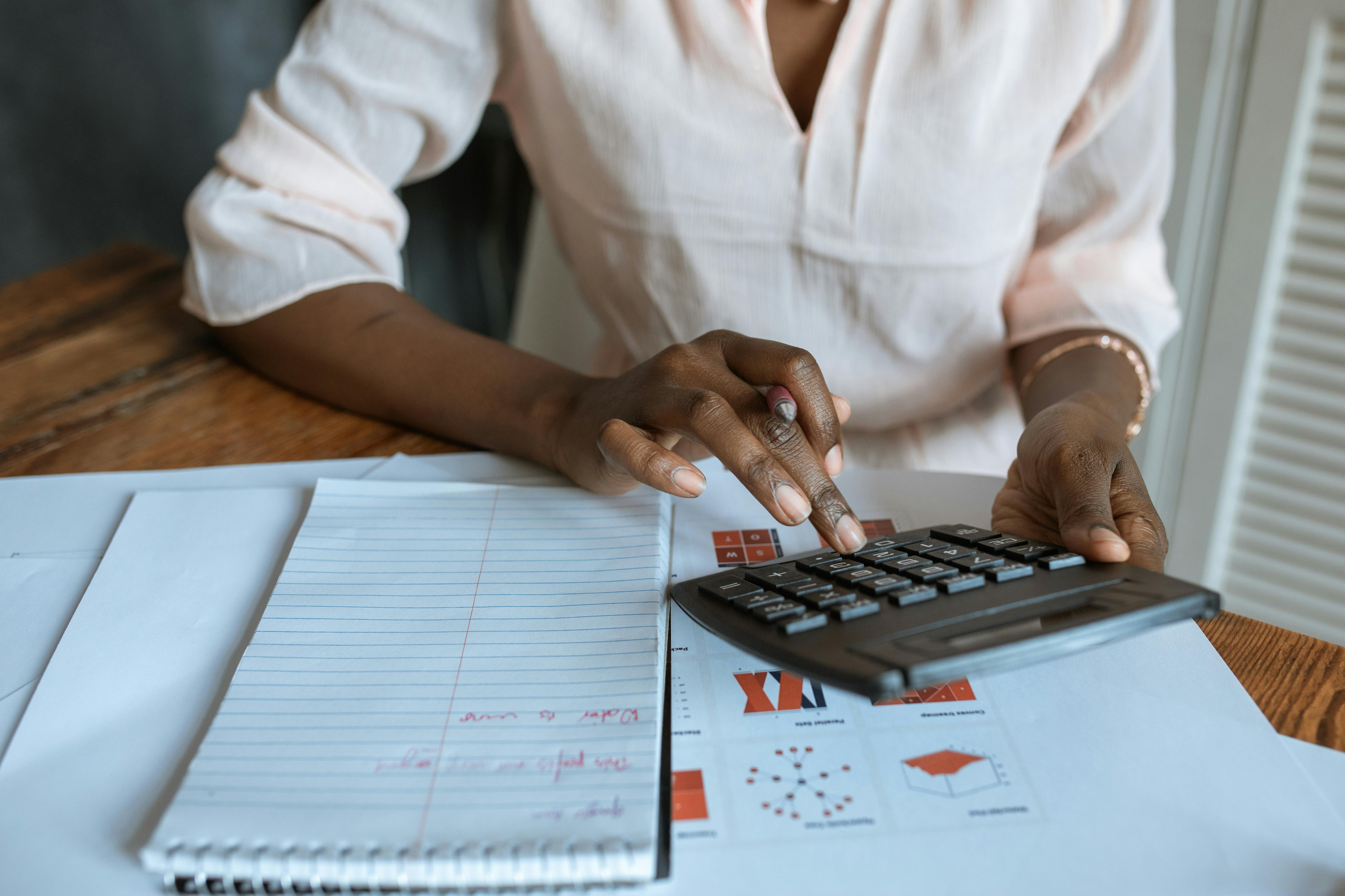 A person using a calculator while taking notes on a notepad with graphs on the table.