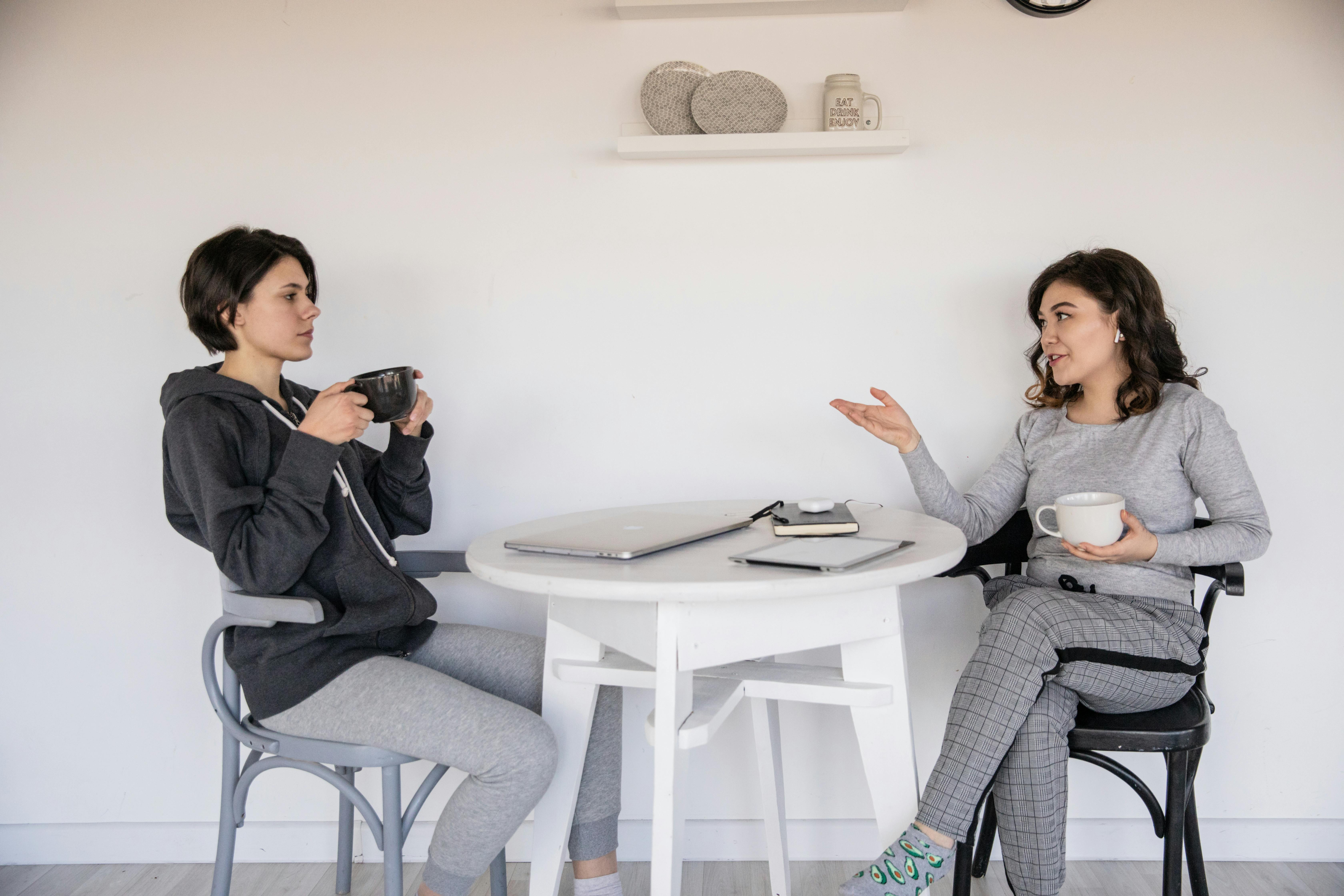 Two women sitting at a table, enjoying coffee and engaging in conversation.