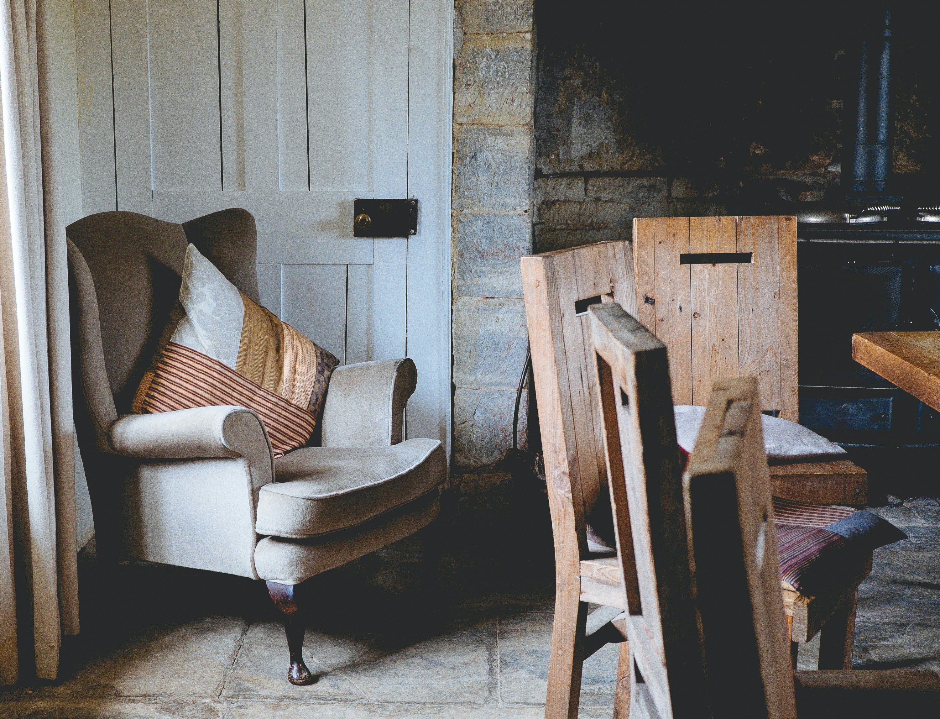 A cozy interior featuring an armchair with cushions and wooden chairs near a dining table.