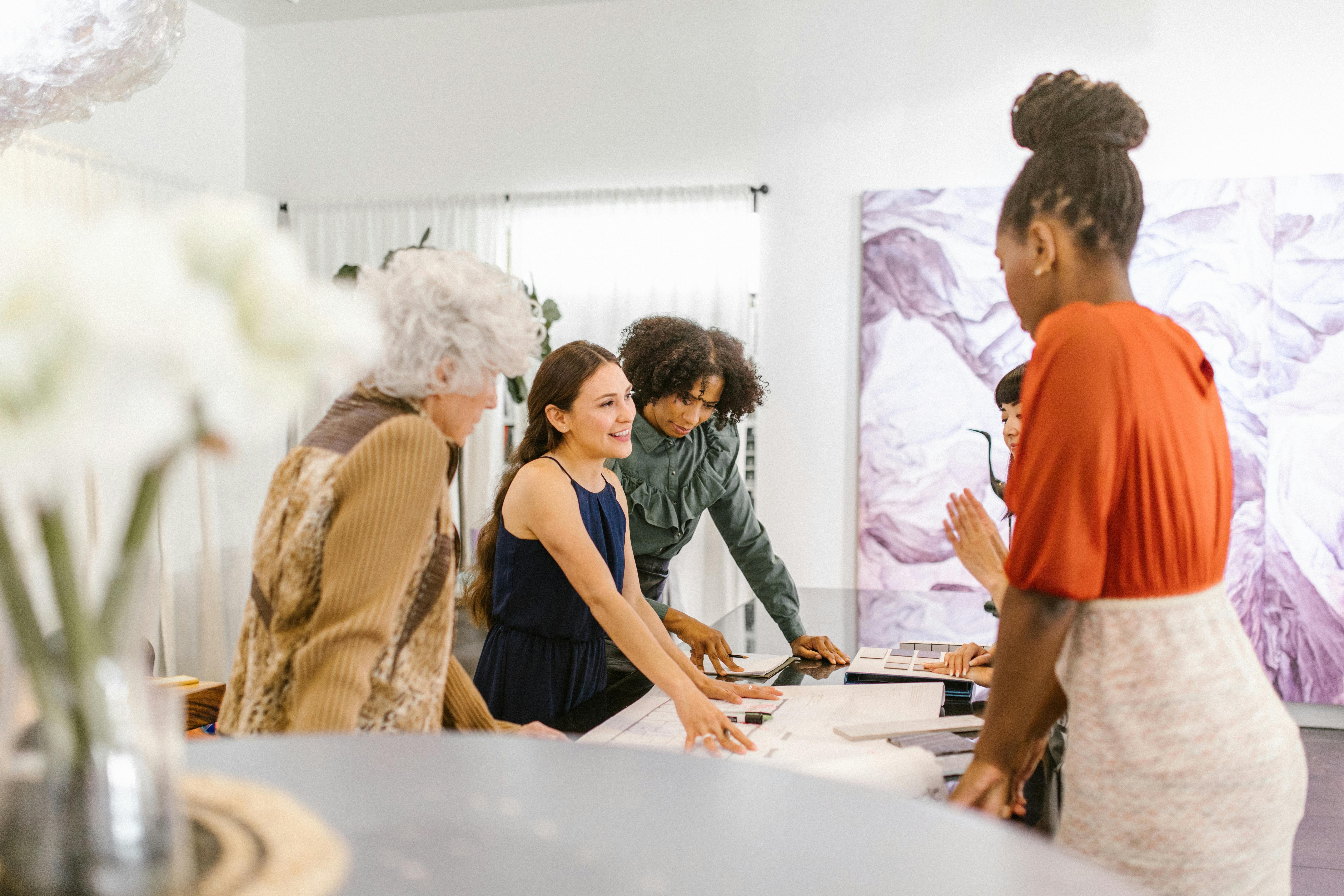 A group of people engaged in a collaborative design meeting around a table covered in materials and samples.