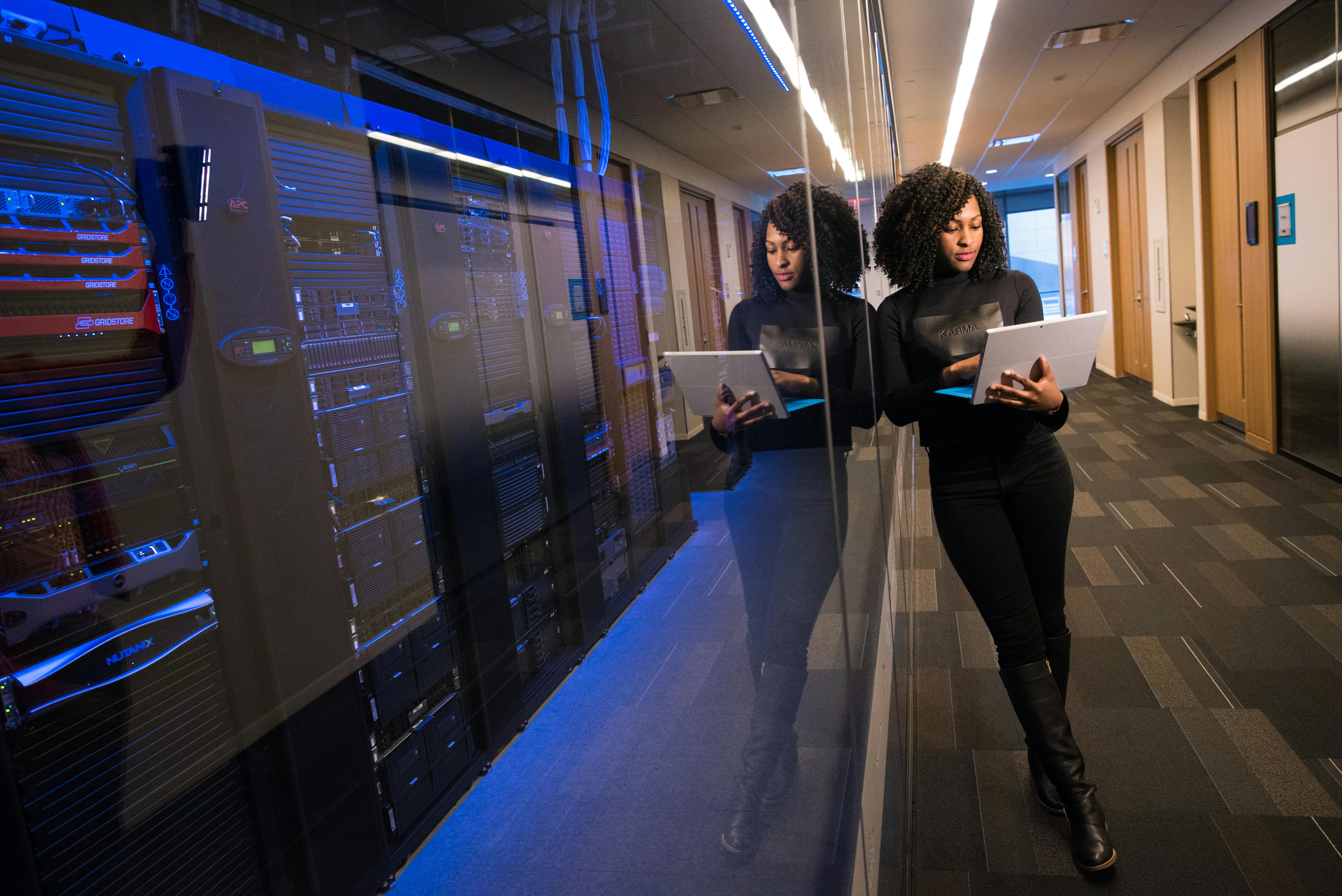 A professional woman using a laptop in a modern data center corridor.