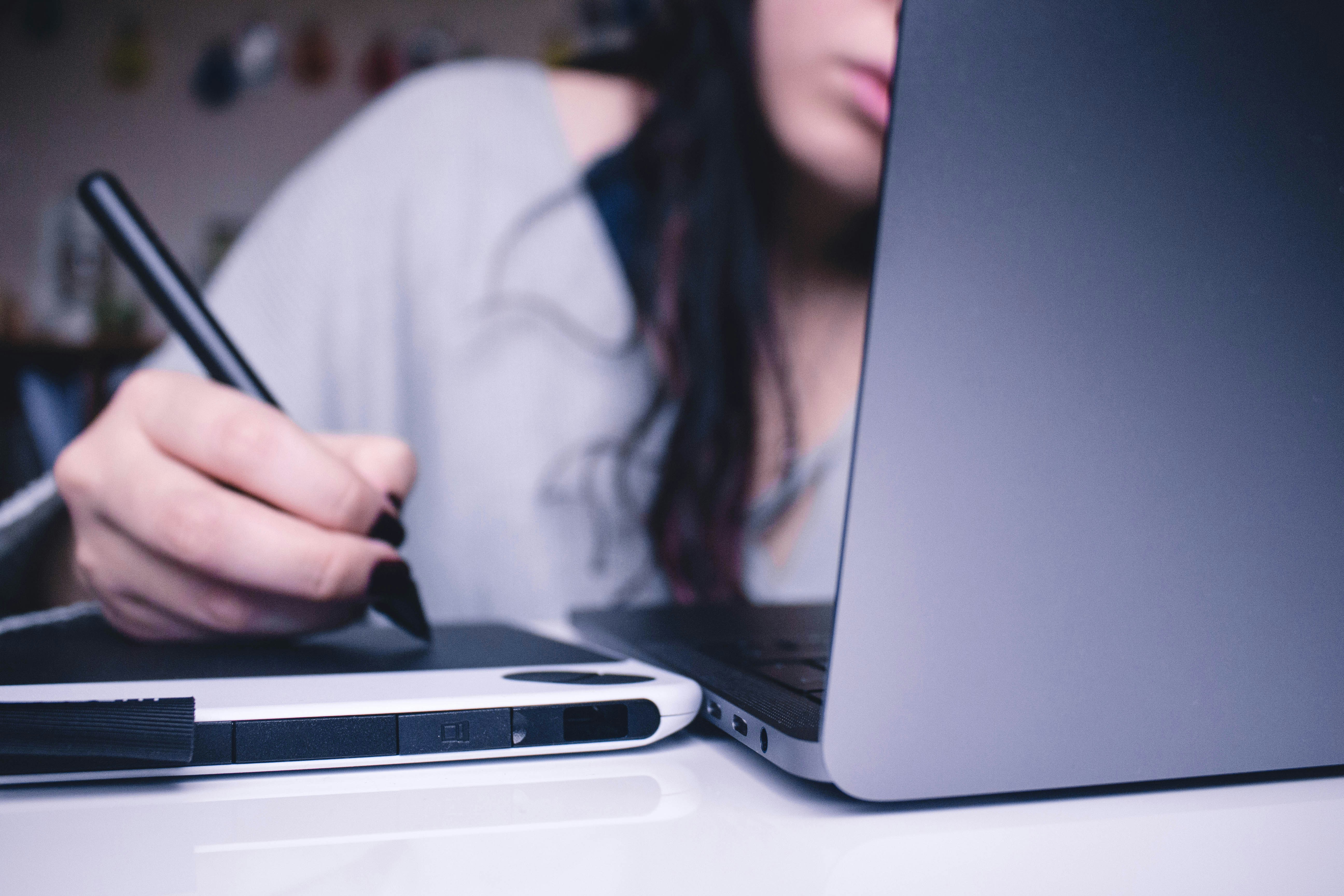 A person using a stylus on a drawing tablet next to a laptop