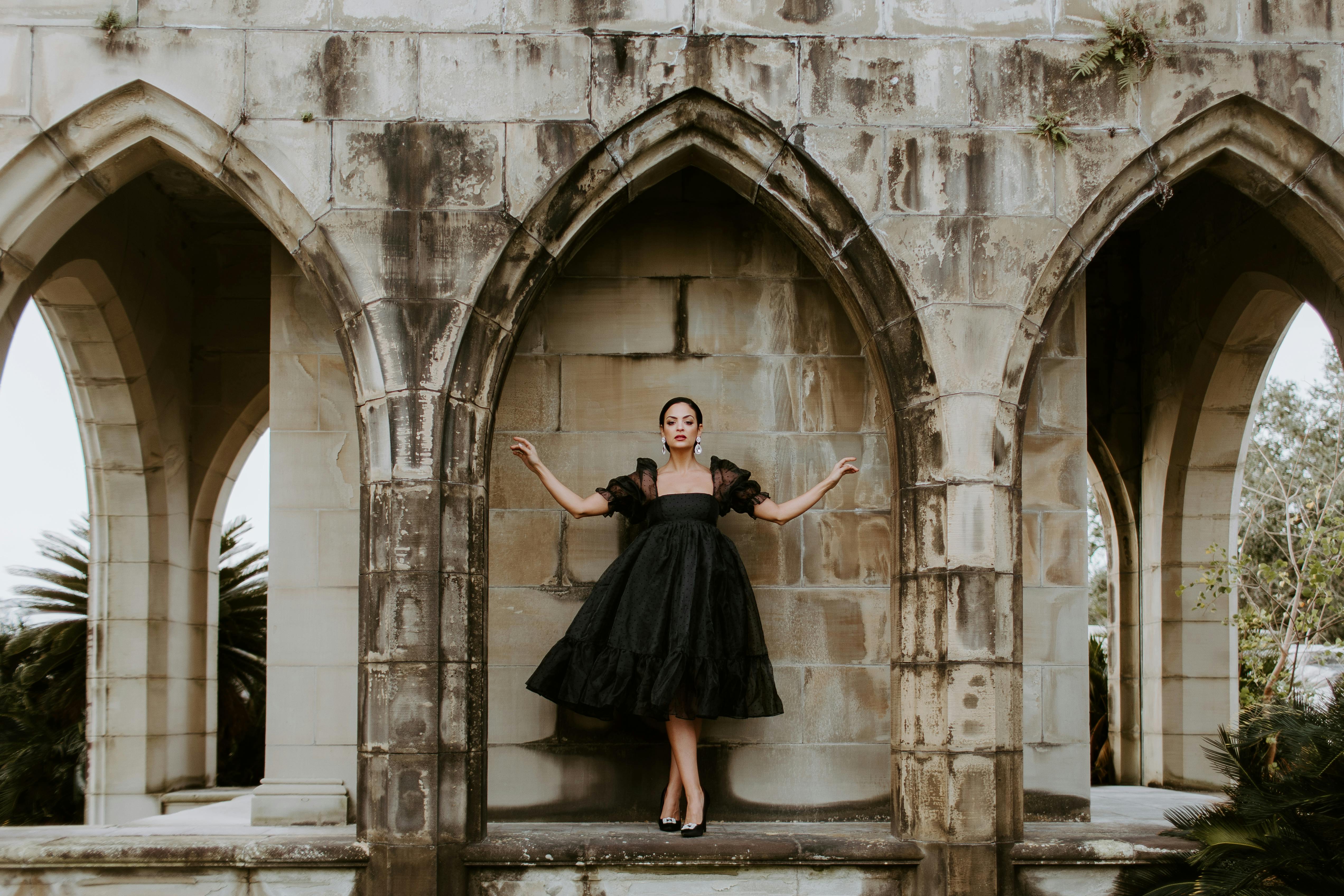 Woman in a black dress posing dramatically inside an architectural archway.