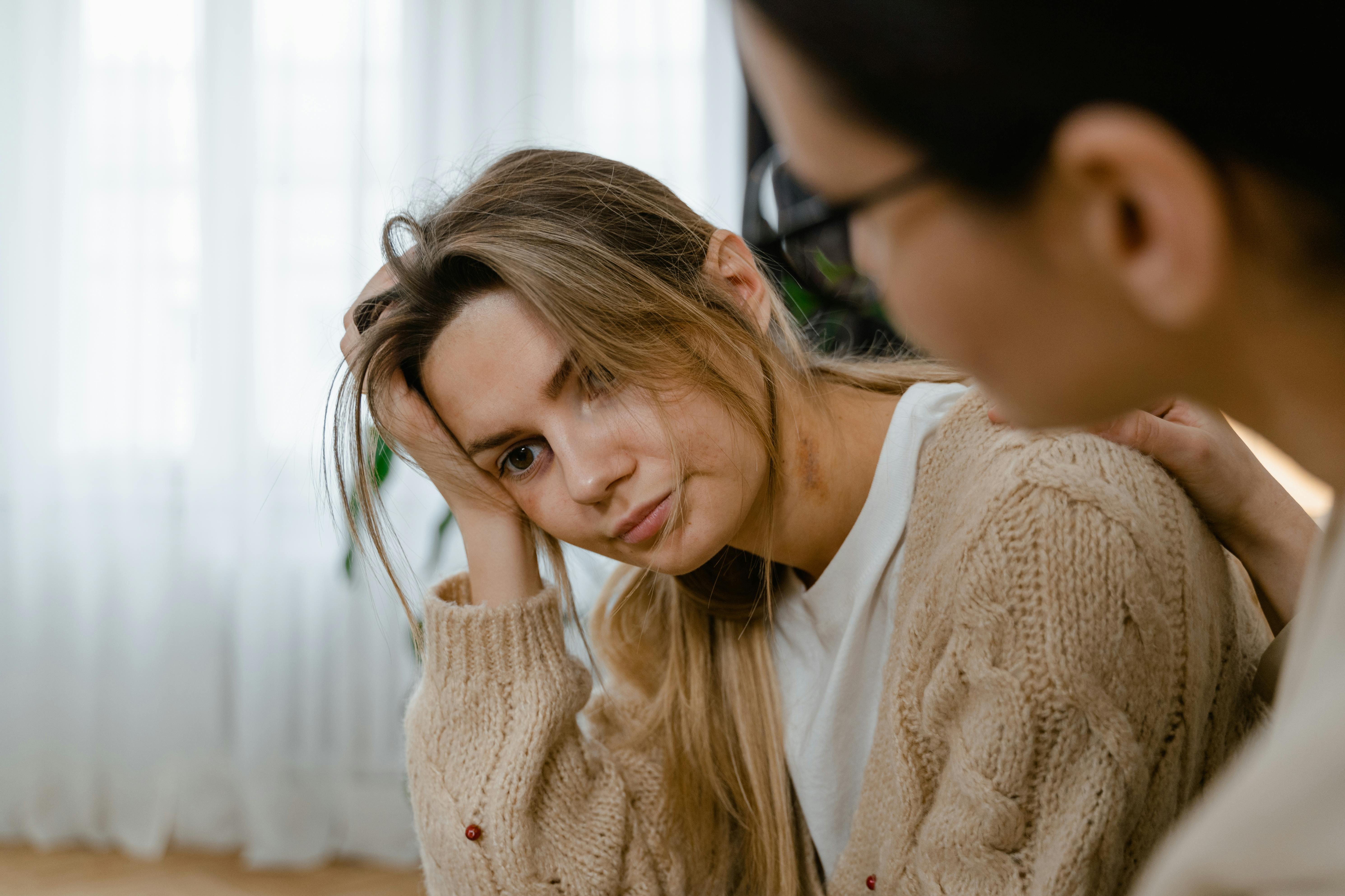 Young woman with long hair looking contemplative while another person comforts her.