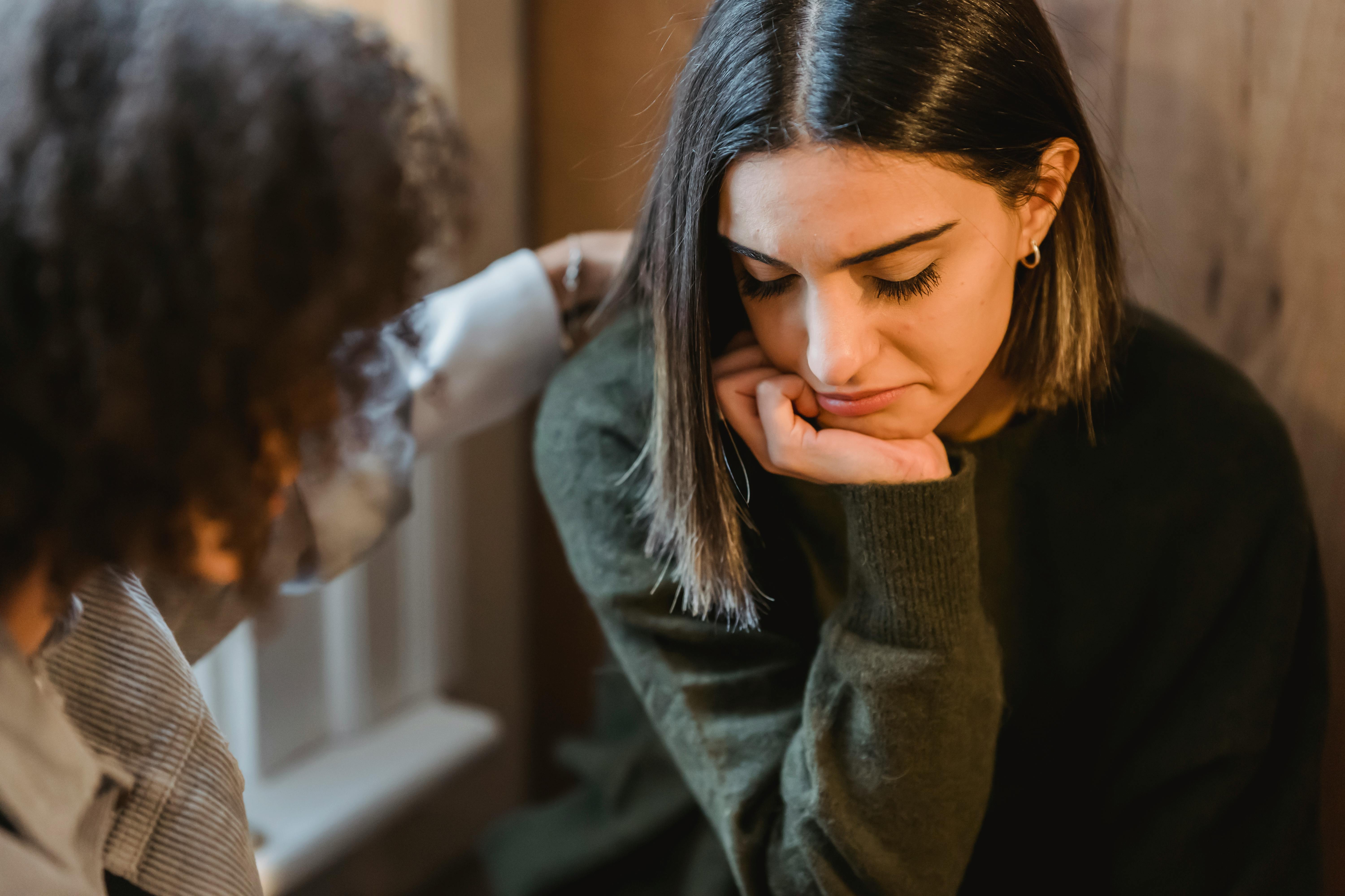 A woman showing concern as she comforts another person, who looks pensive and sad.