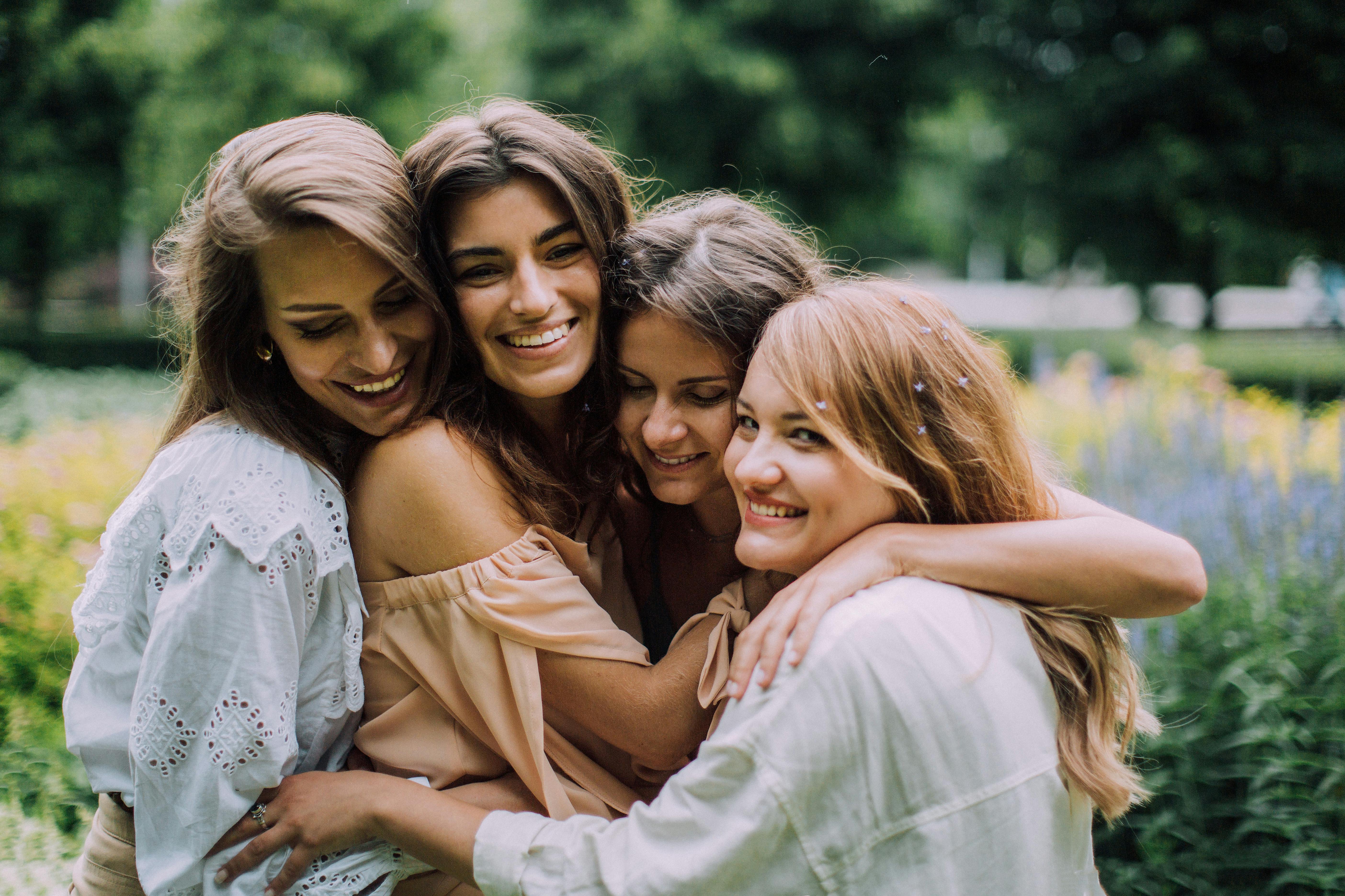 Four smiling women embracing each other in a lush green park.