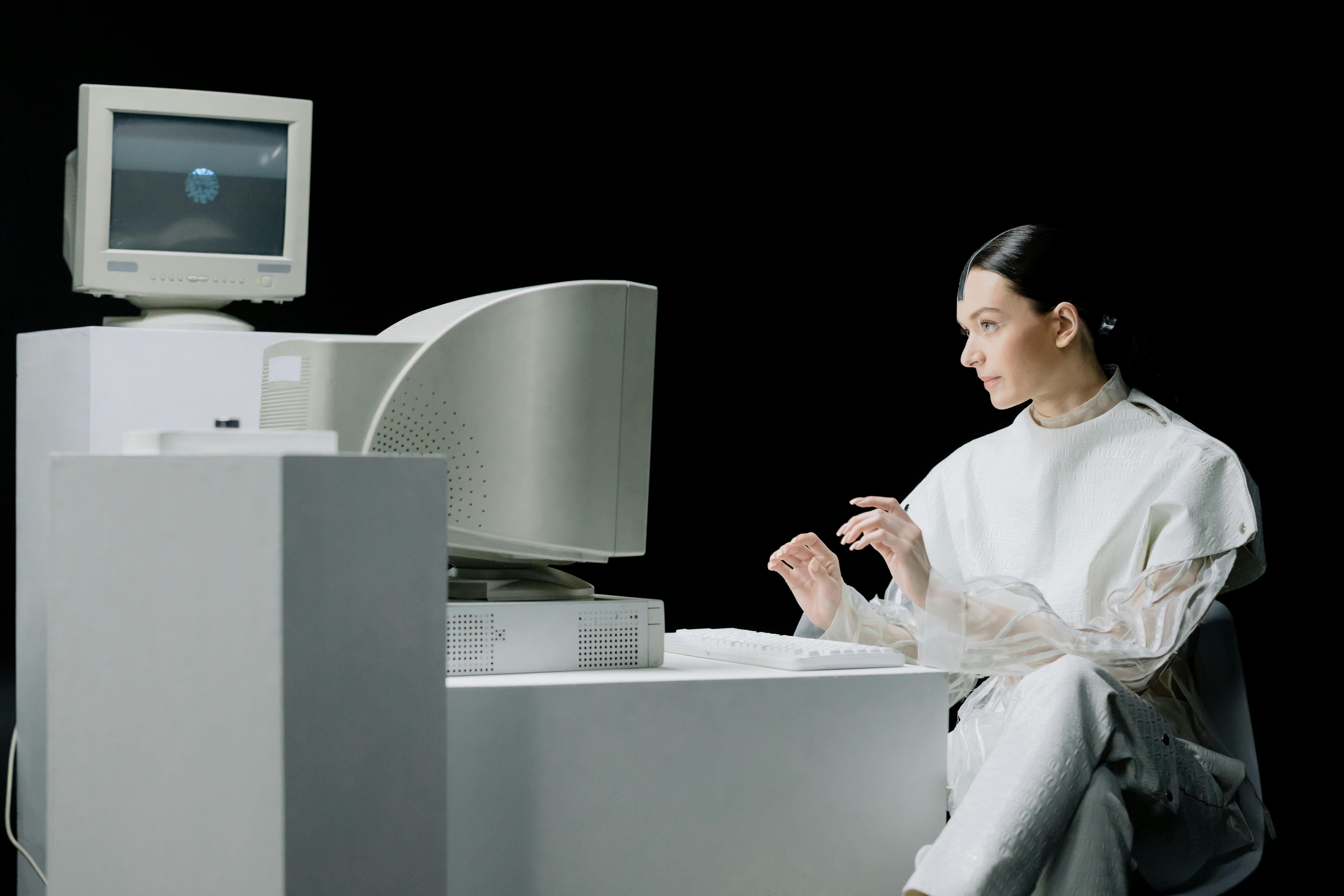 A person in a white outfit using a retro computer in a dark setting.