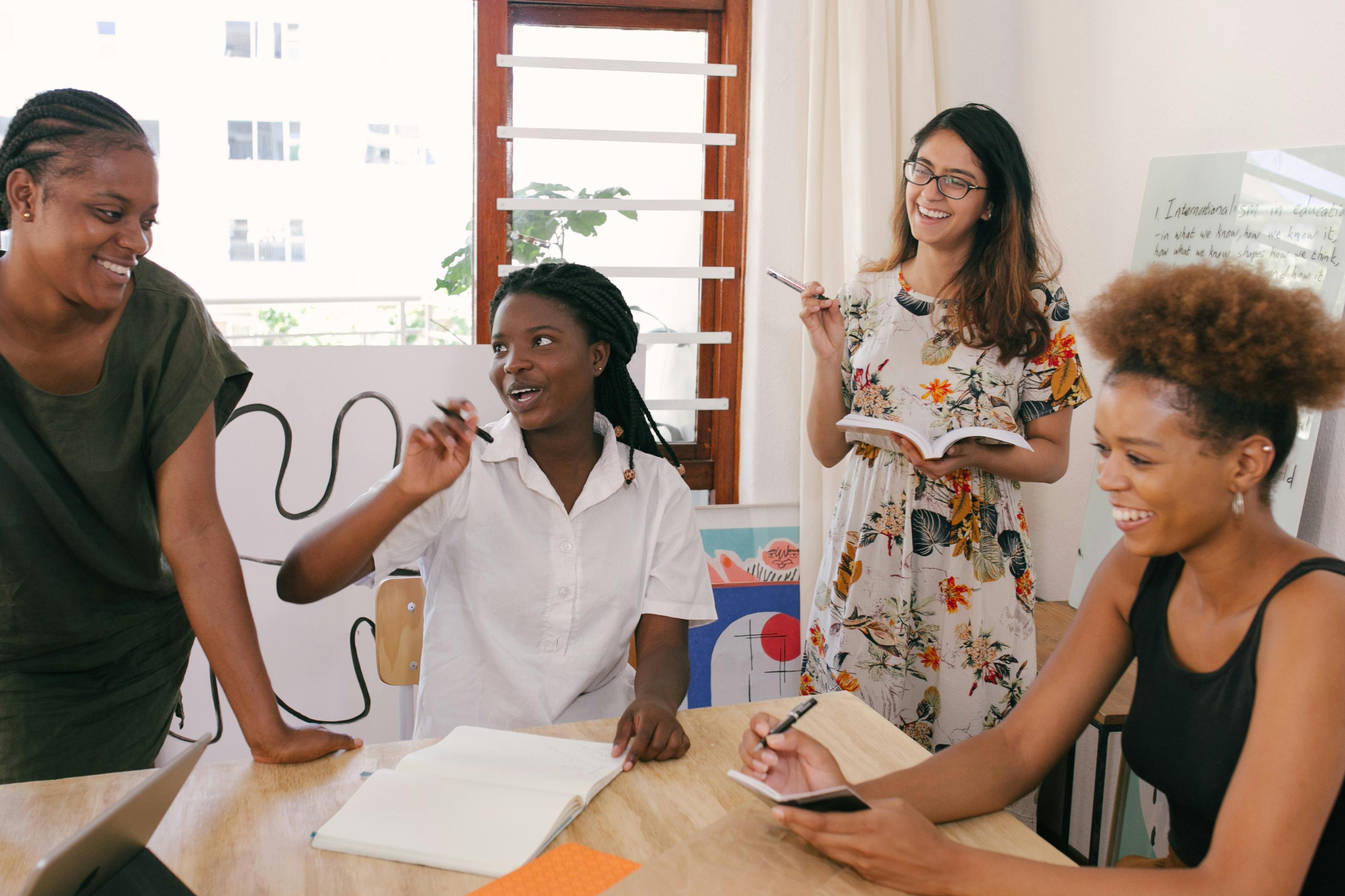 A group of four women engaged in a lively discussion around a table with notebooks and pens.