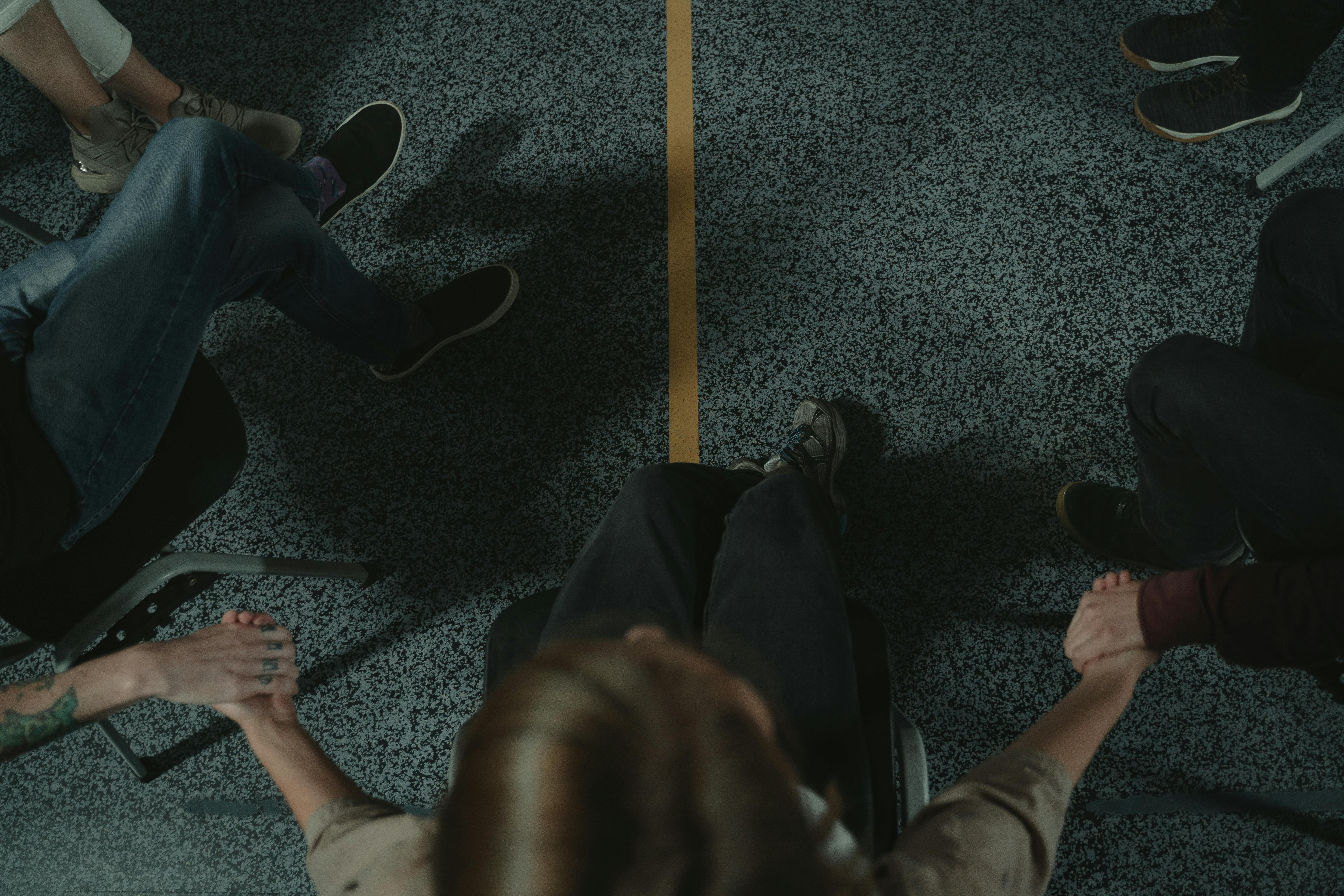 A group of people holding hands, seated in a circle, viewed from above.