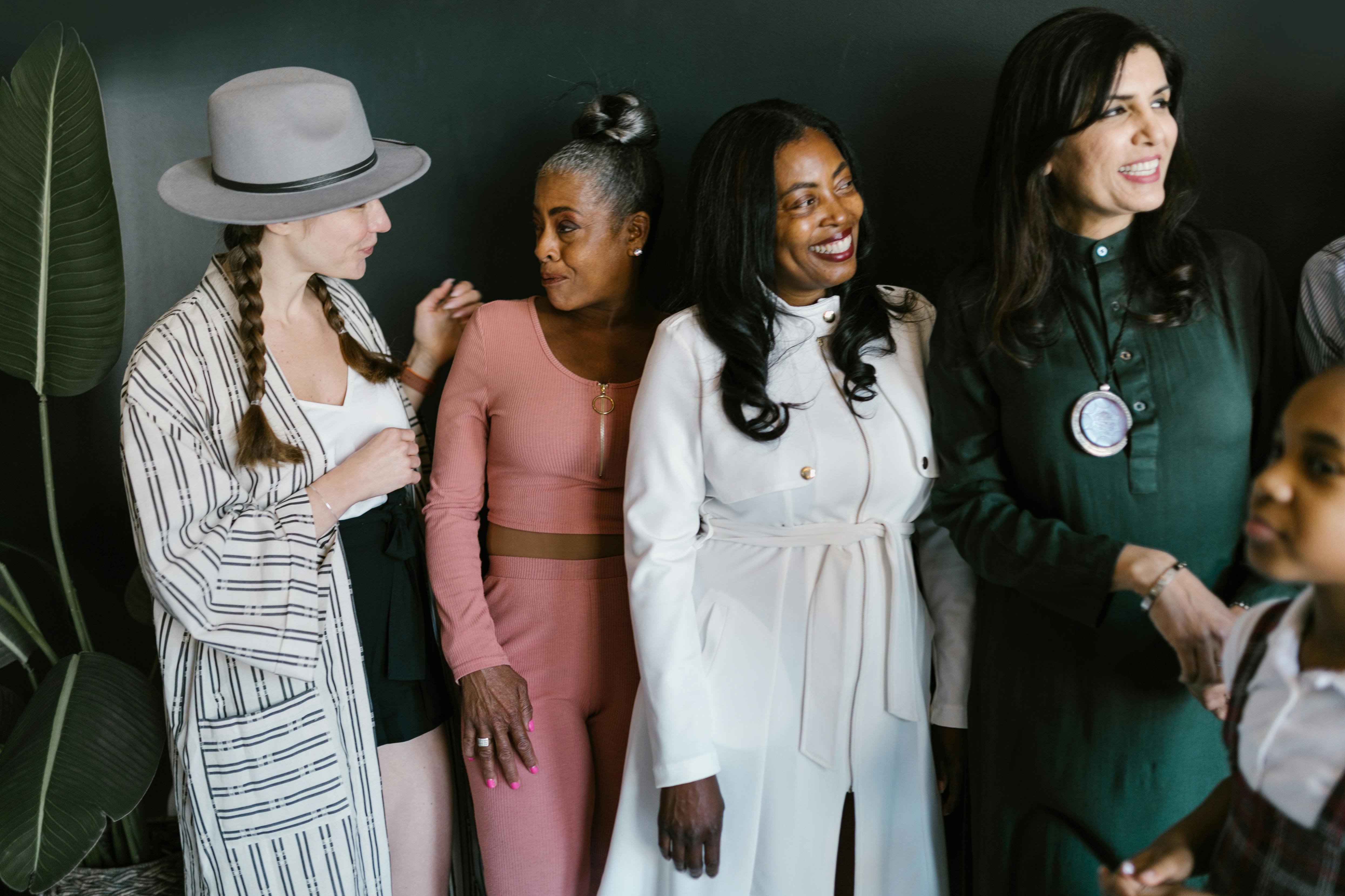 A group of diverse women smiling and posing together, showcasing different styles of clothing.