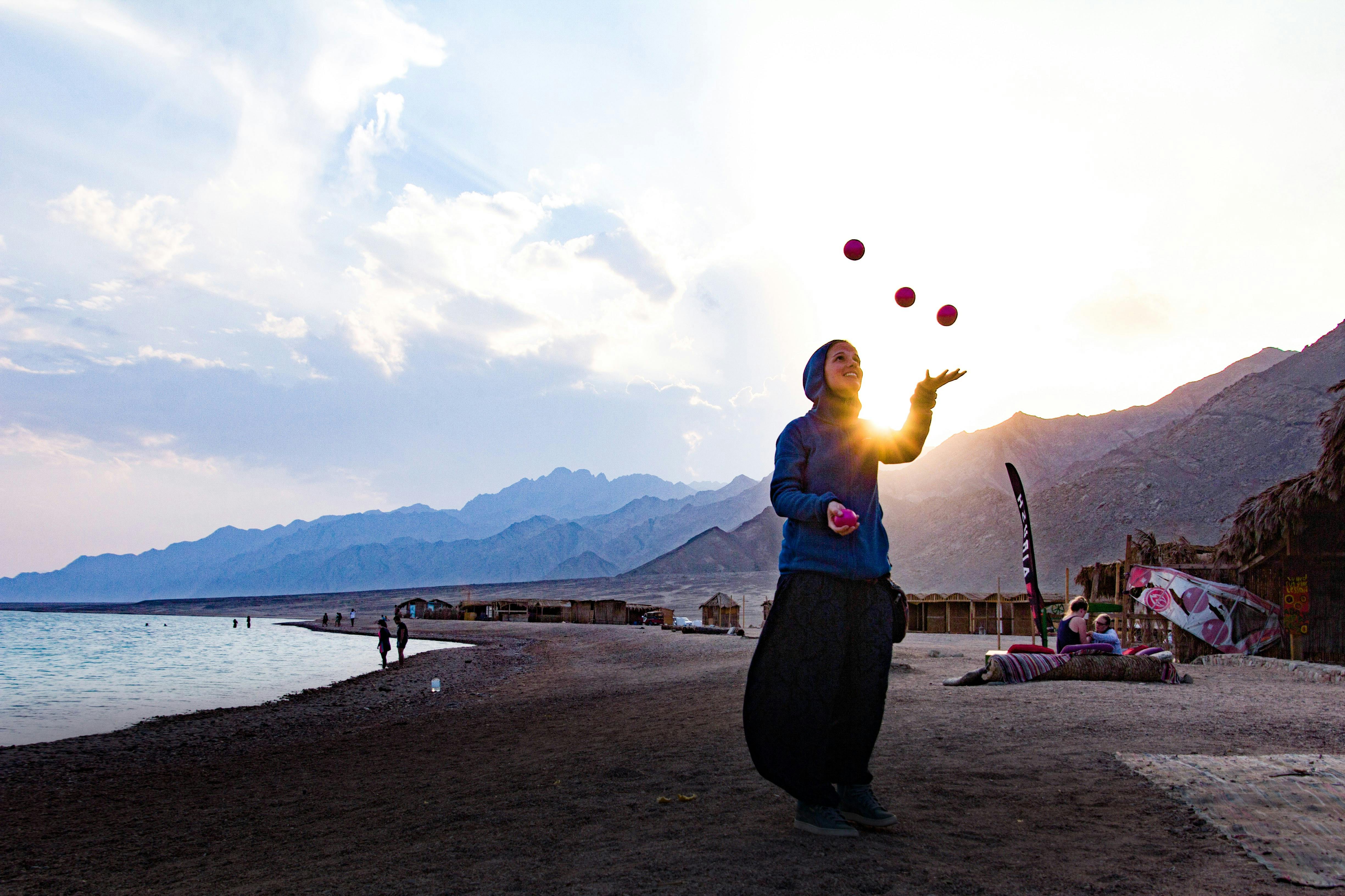 A person juggling balls against a backdrop of mountains during sunset.