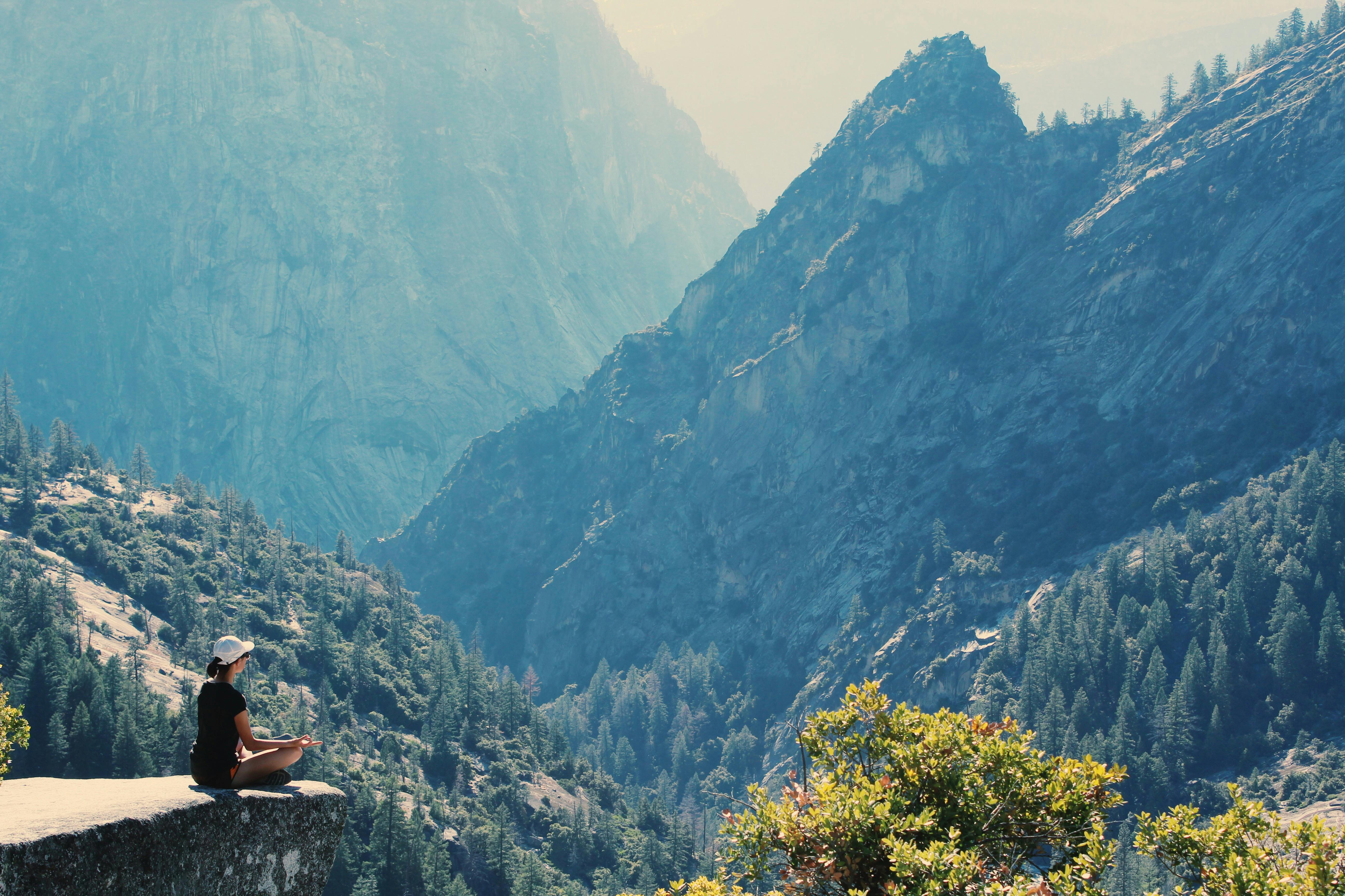 A person meditating on a rock in a mountainous landscape.