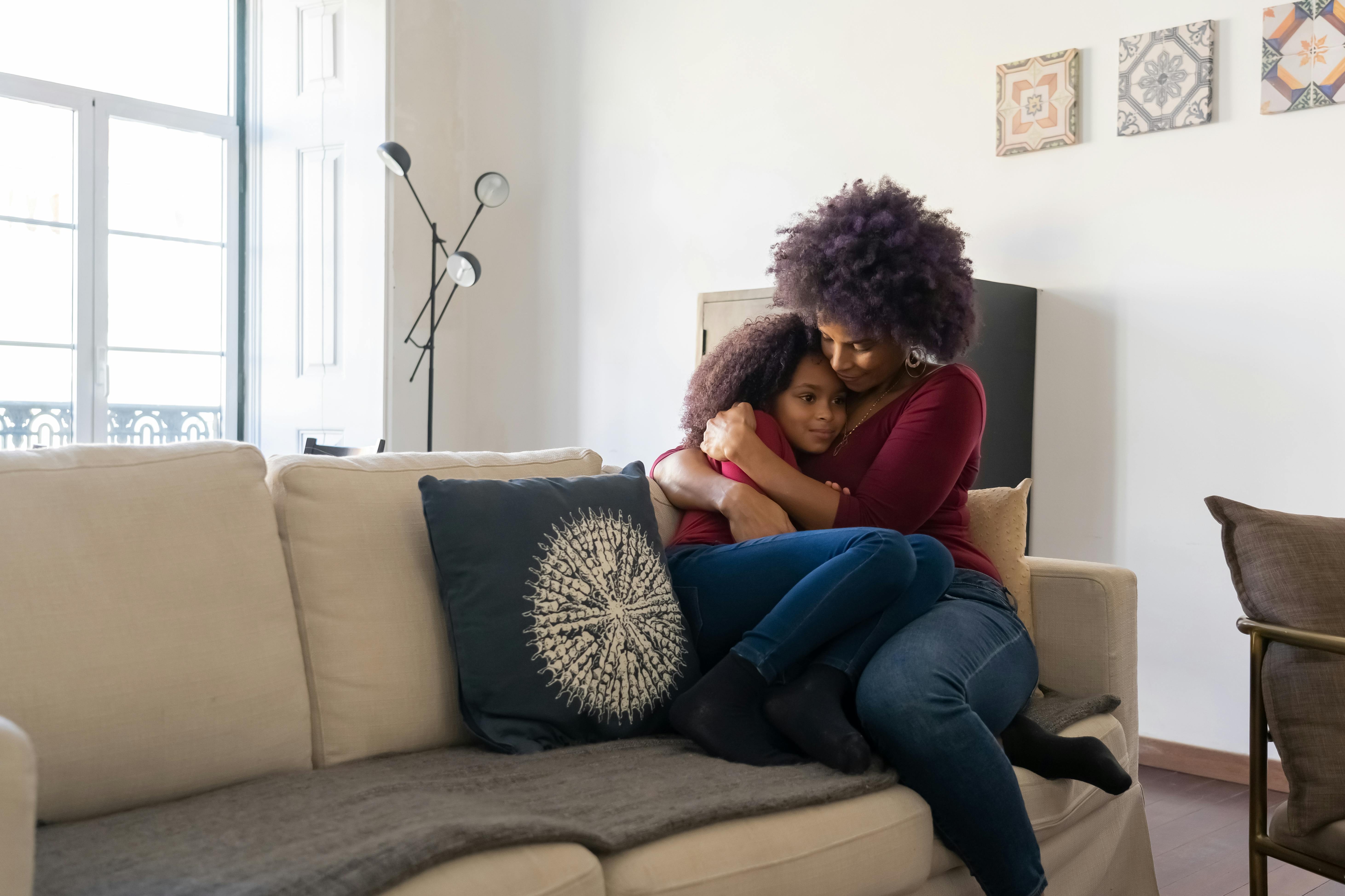 A mother hugging her daughter on a couch in a cozy living room.