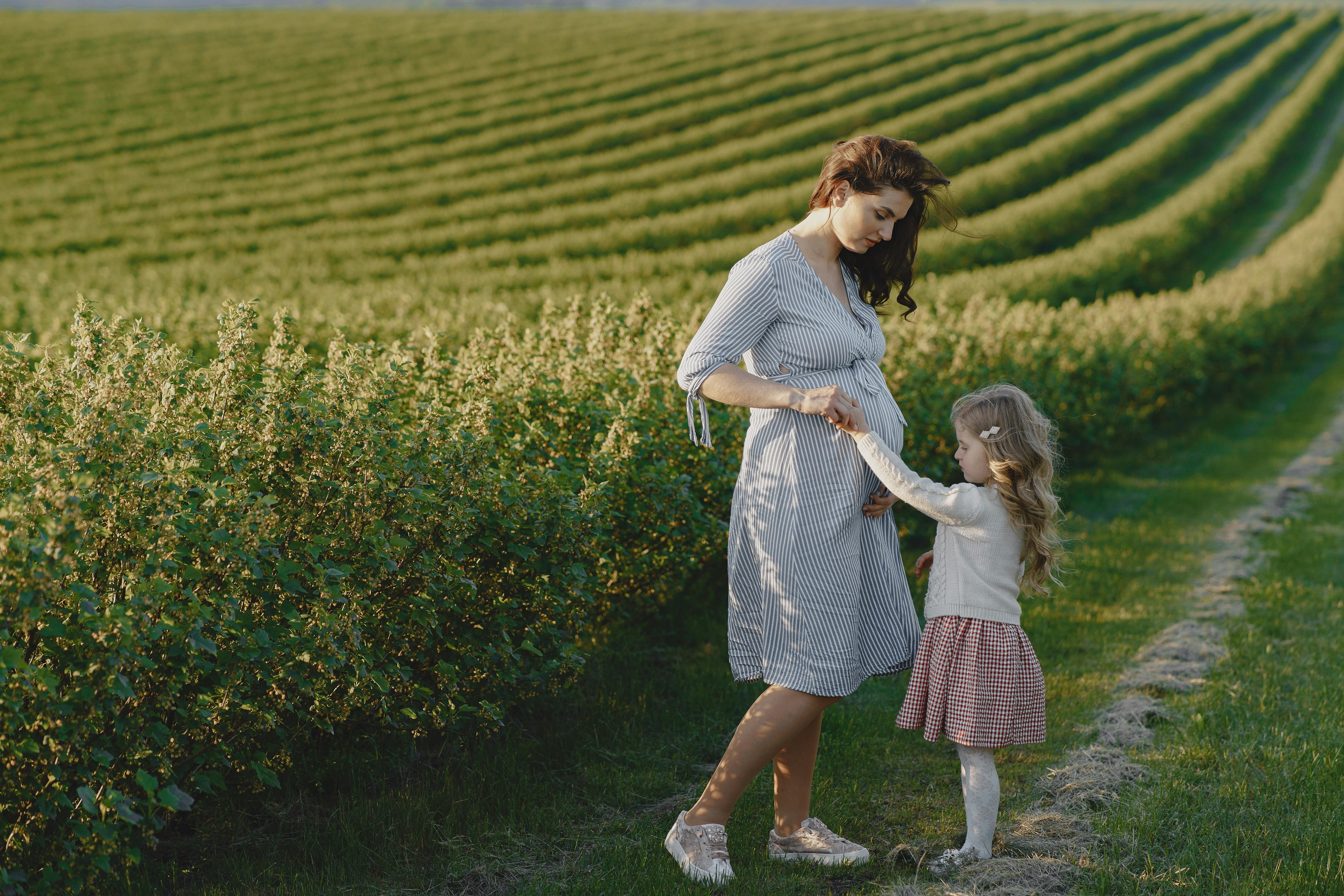 A pregnant woman and a young girl interacting in a green field