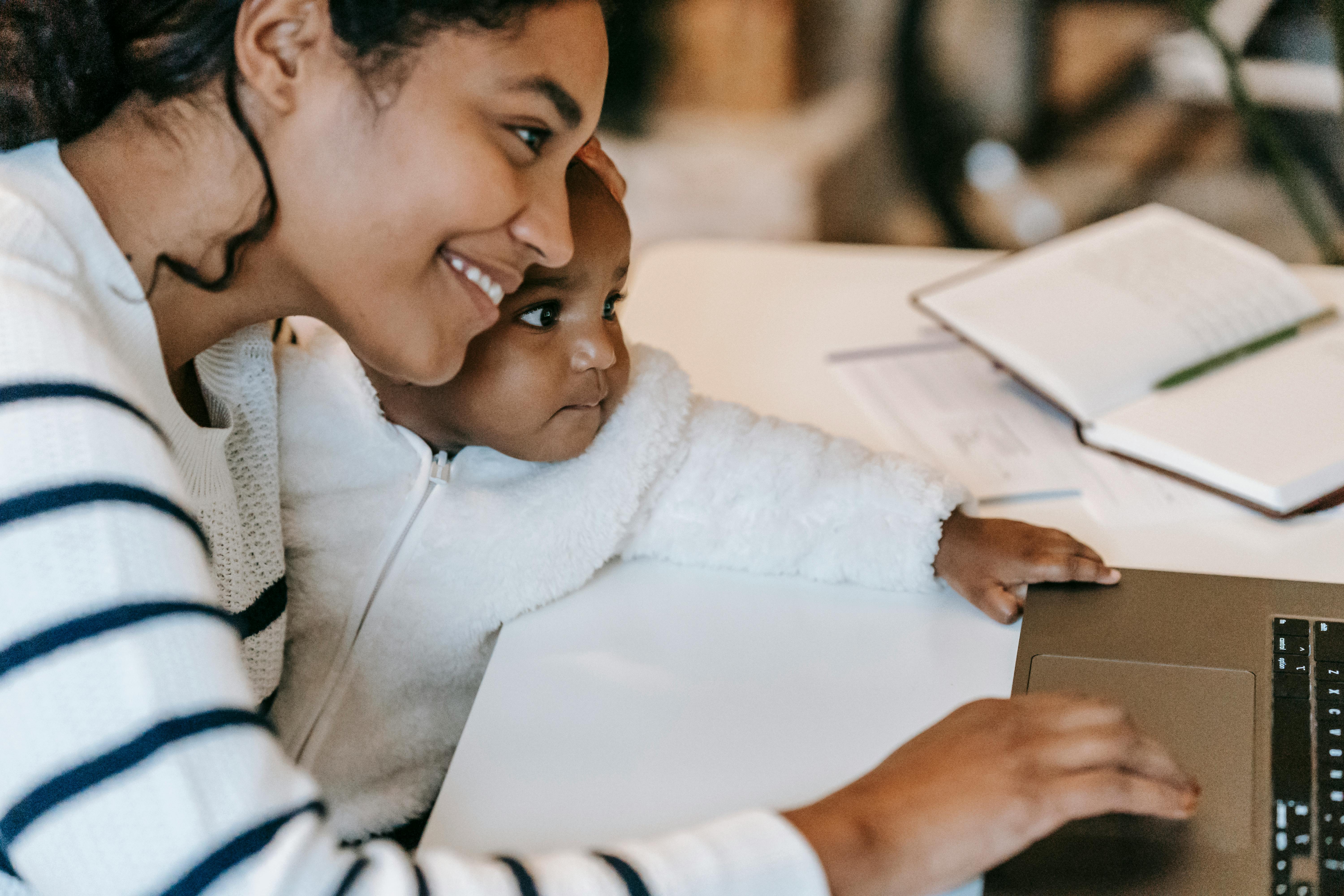 A mother and her child sitting together at a table using a laptop.