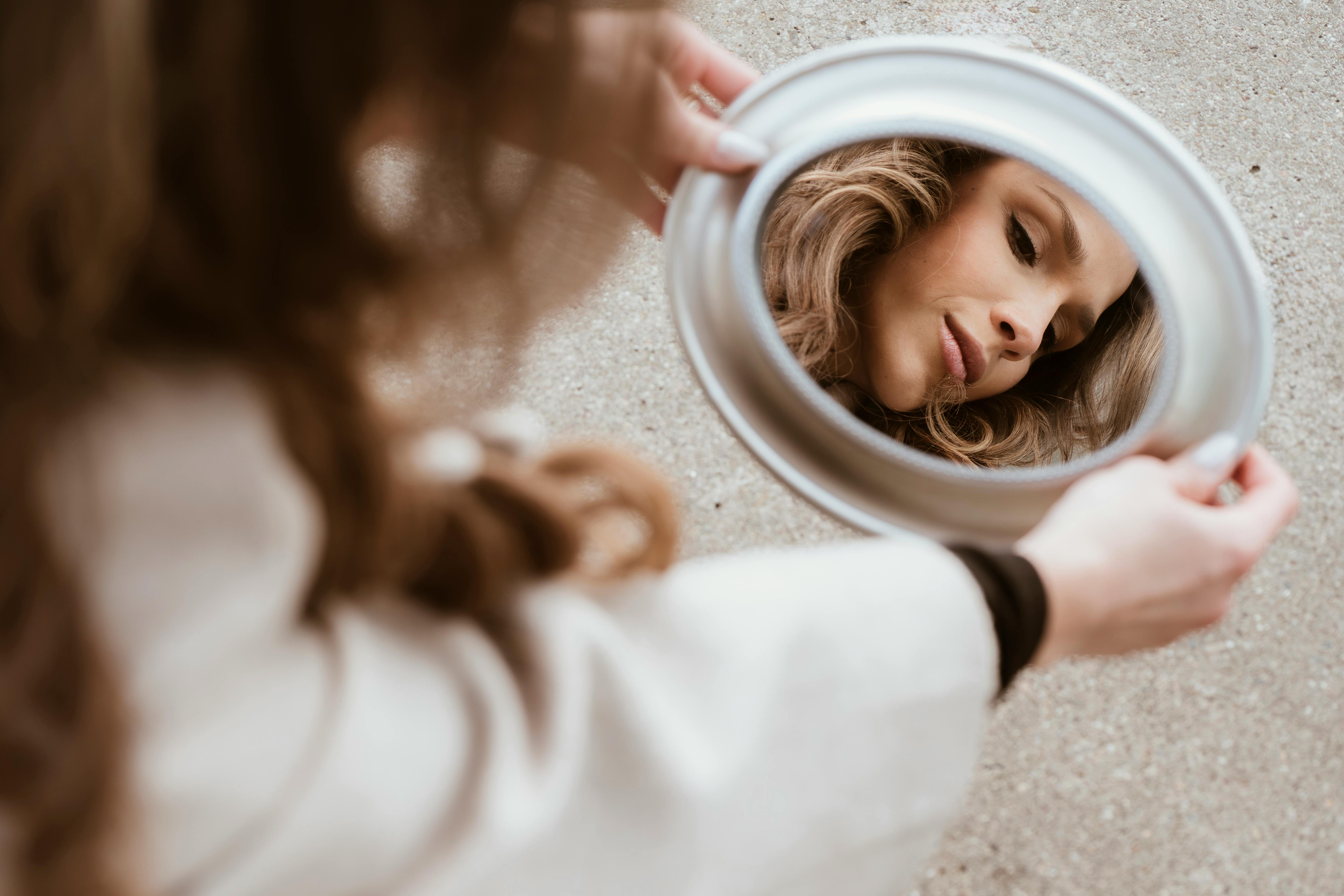 A woman looking at her reflection in a handheld mirror.