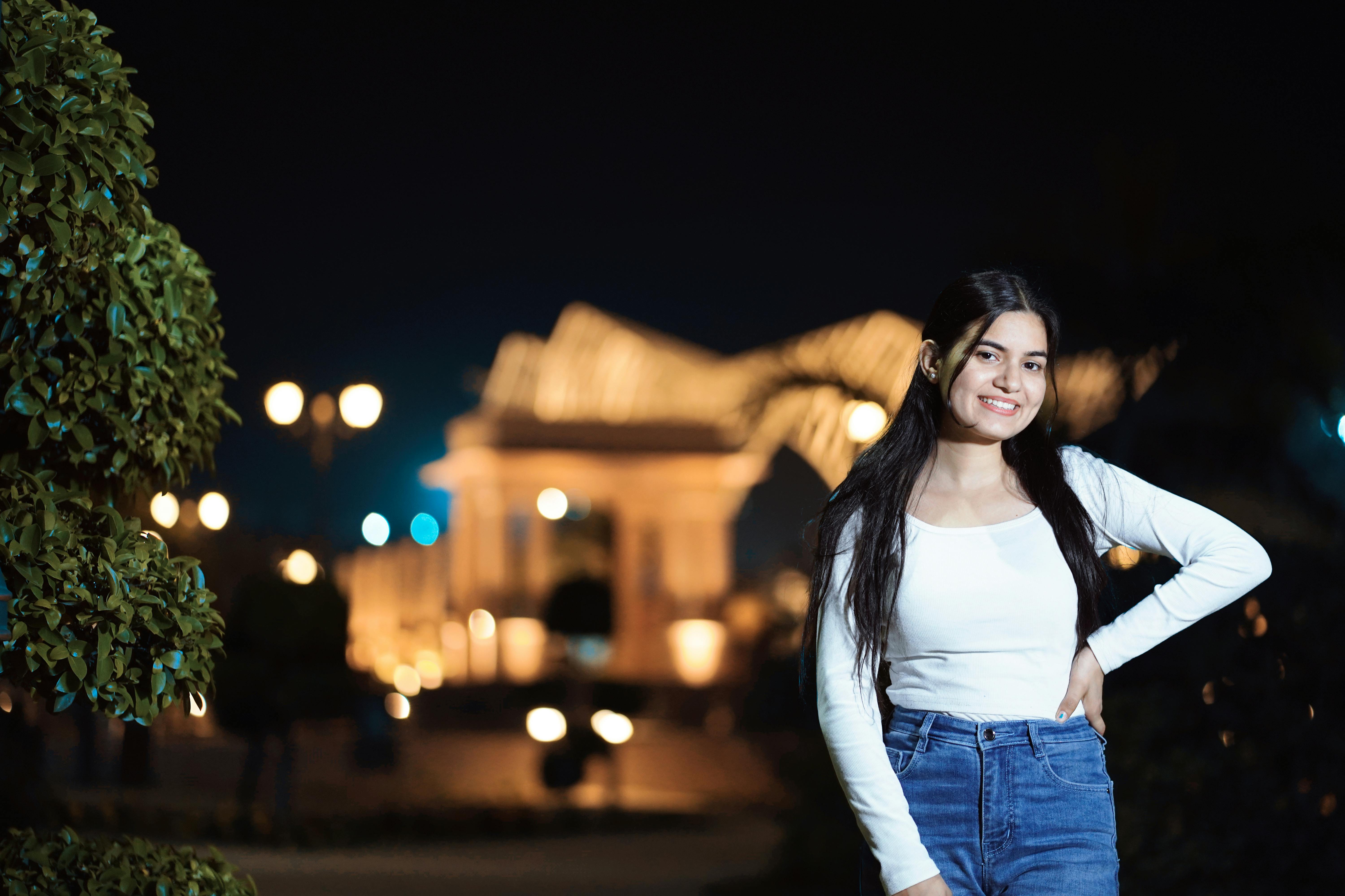 A young woman smiling in a park at night, with decorative lights in the background.