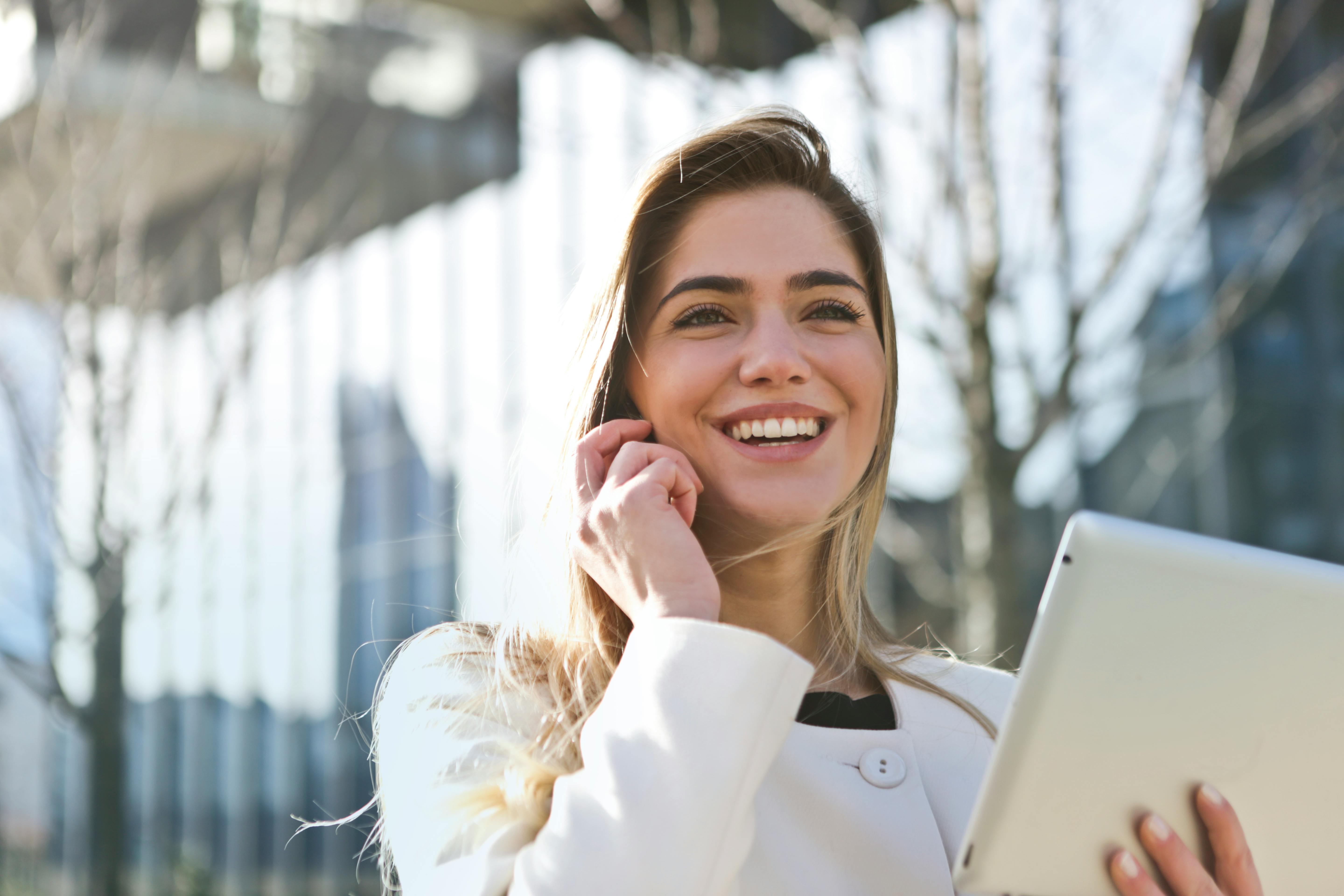 Woman smiling while holding a tablet outdoors