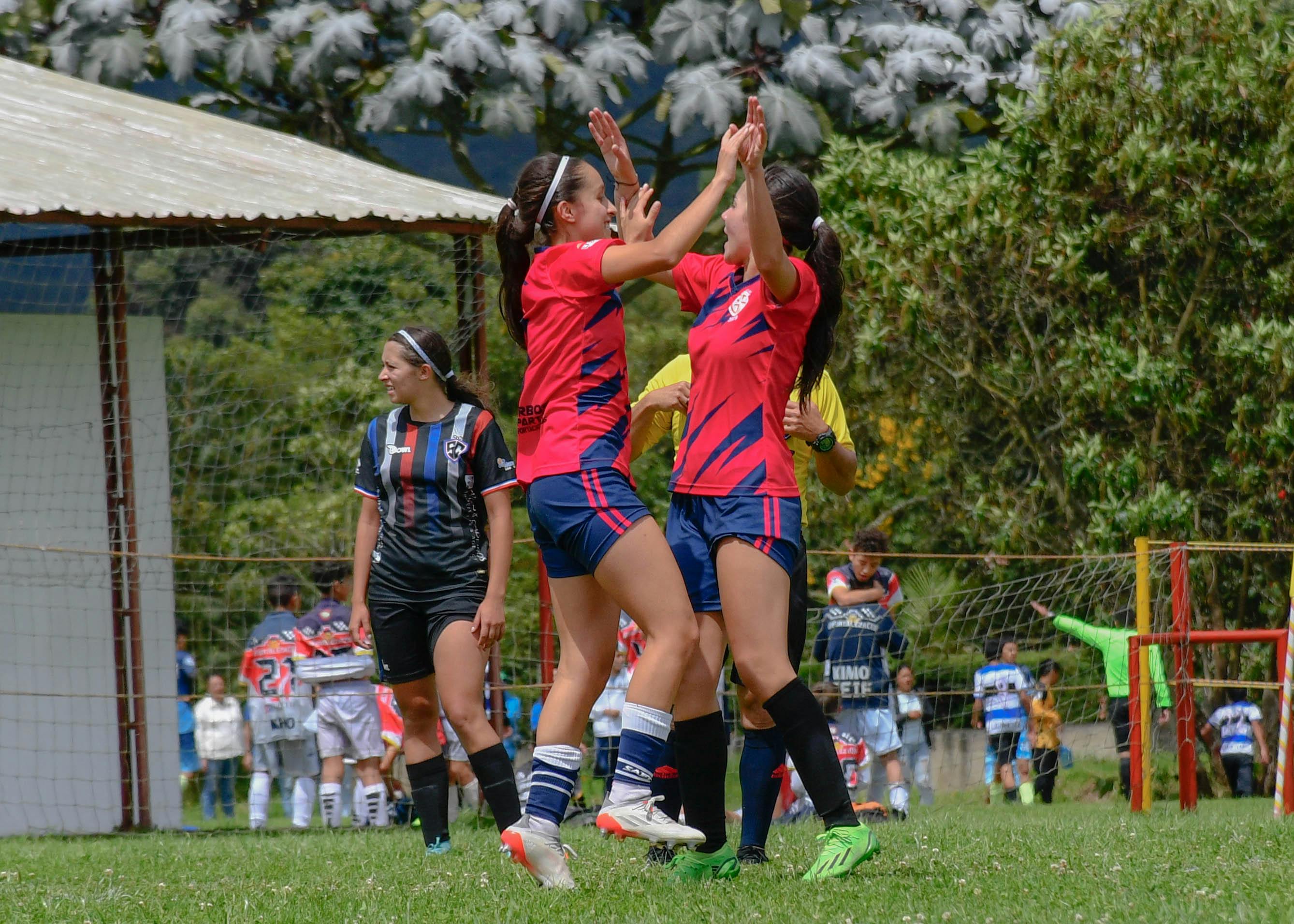 Two female soccer players celebrating a goal on the field.