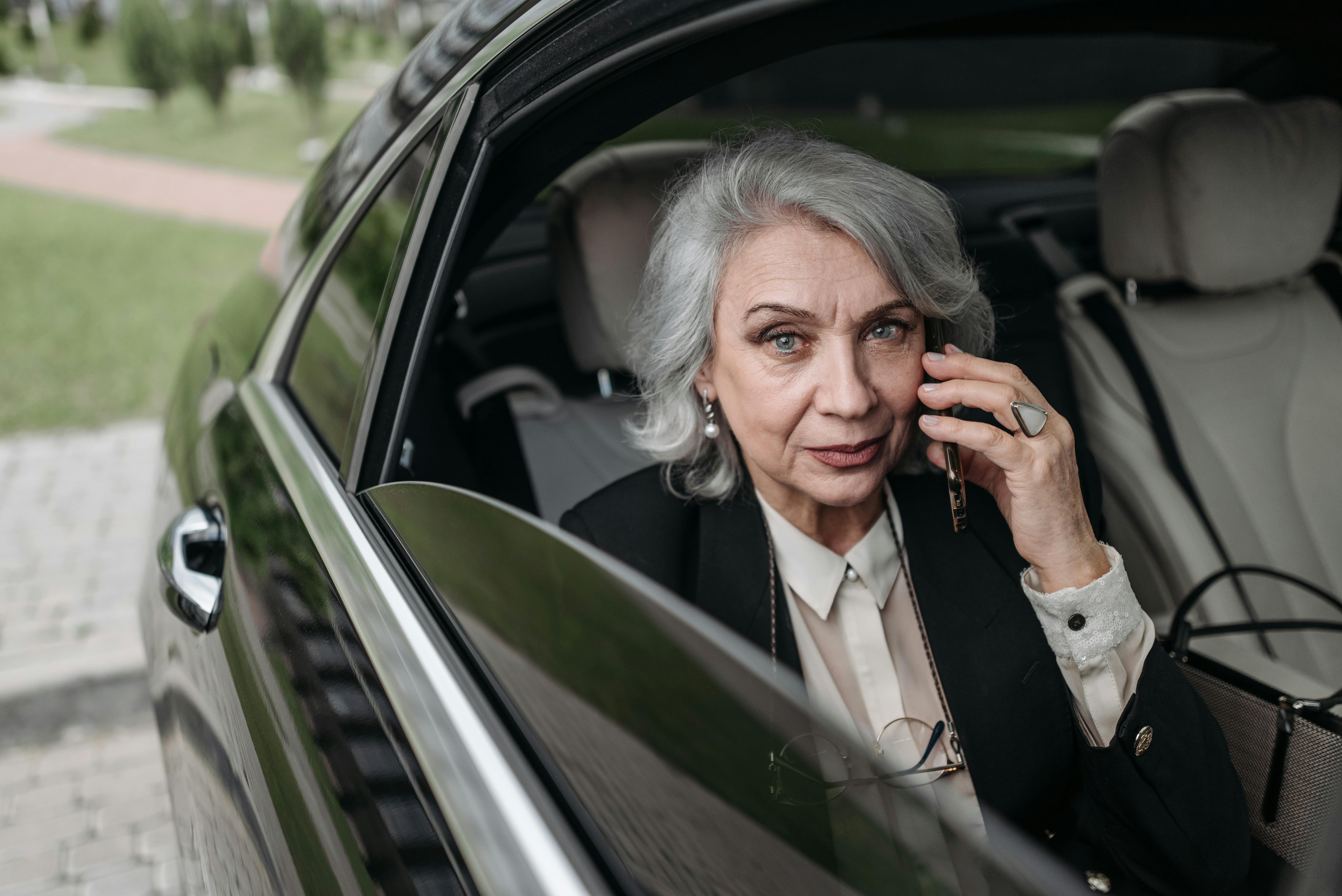 A mature woman sitting in a car, speaking on her mobile phone.