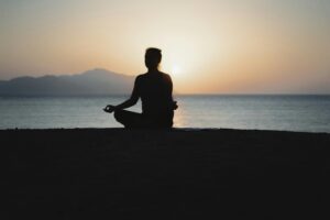 Silhouette of a person meditating by the sea at sunset.