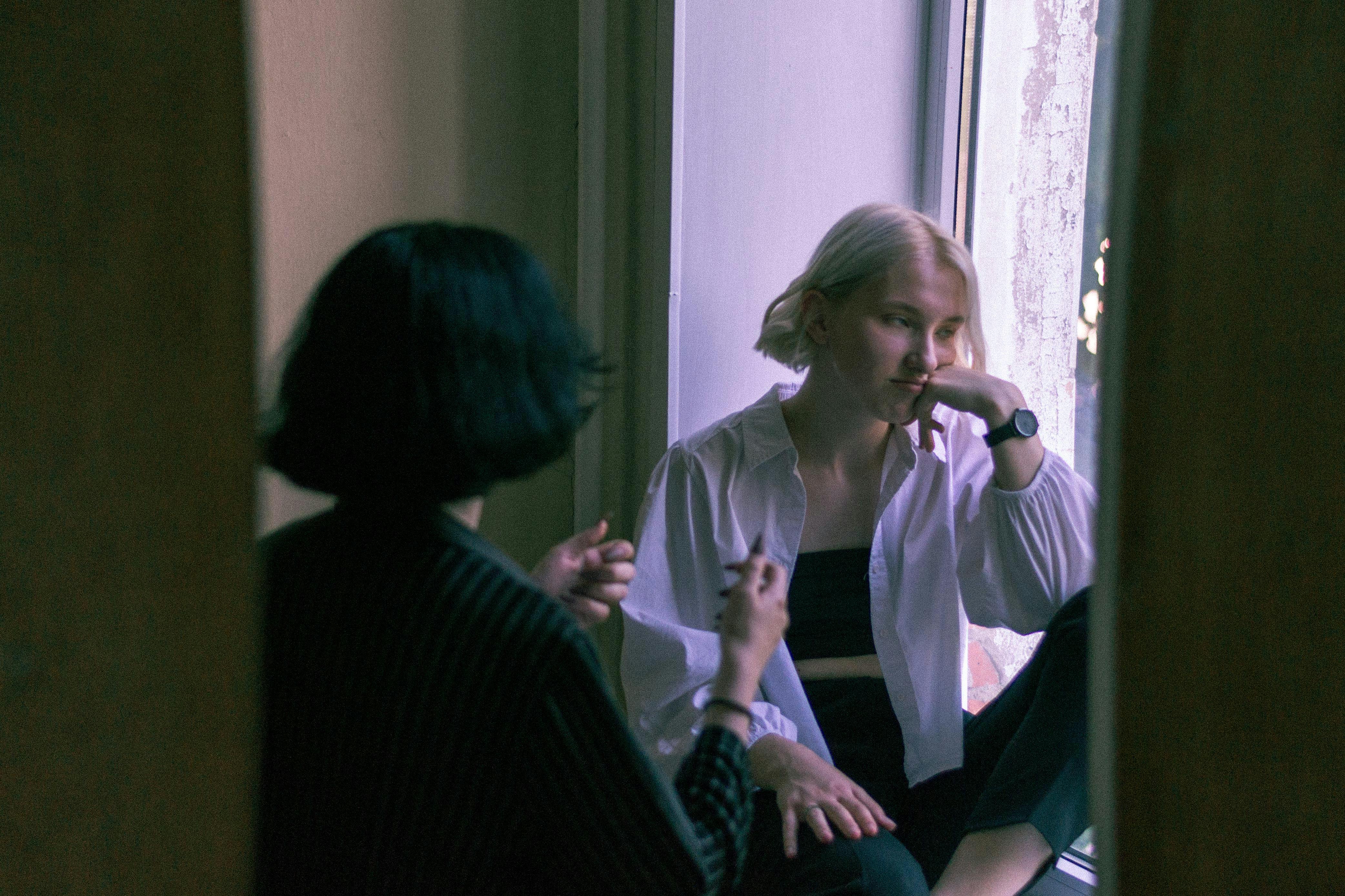 Two young women engaged in a thoughtful conversation by a window.