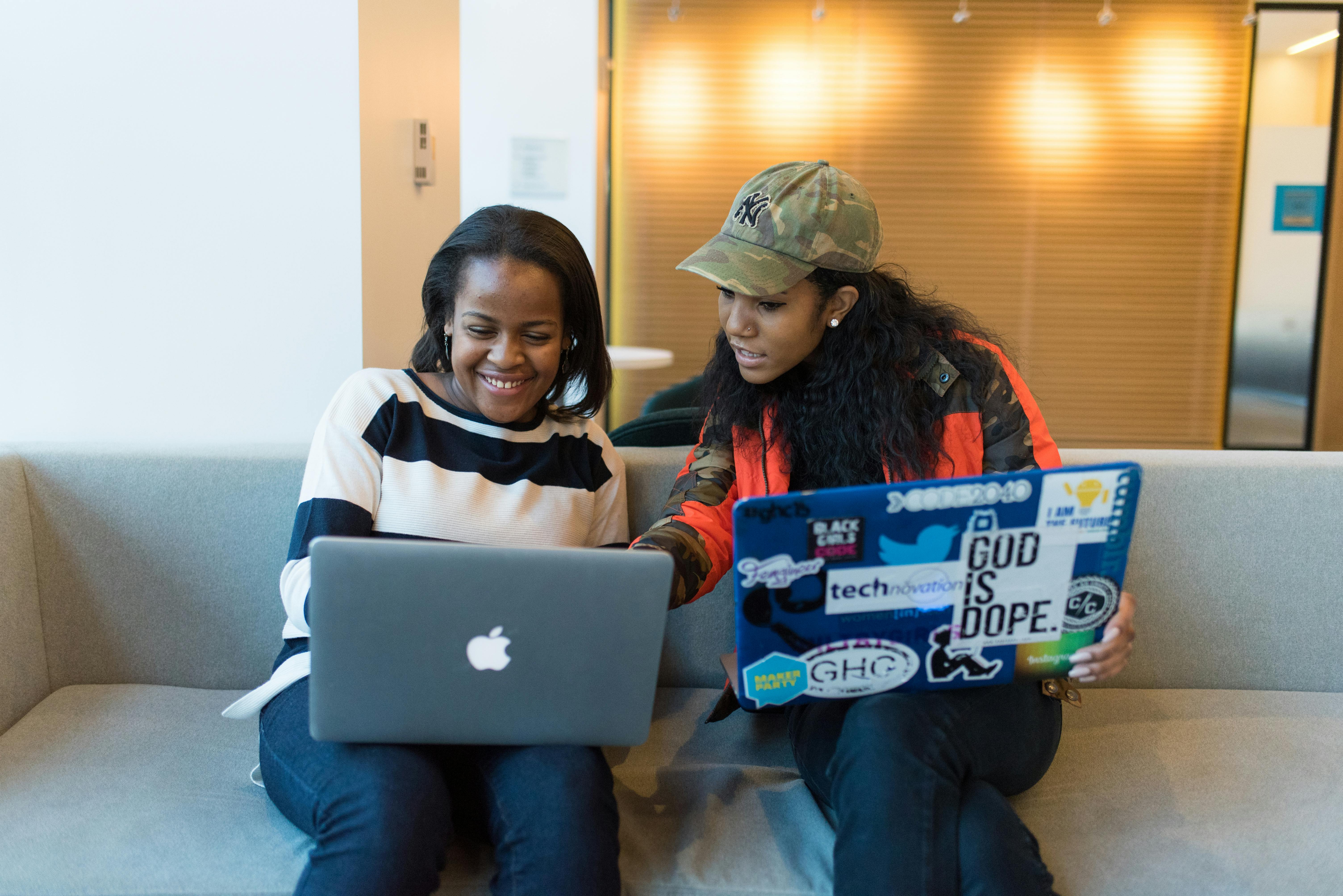 Two women engaged in a collaborative work session on laptops in a casual setting.