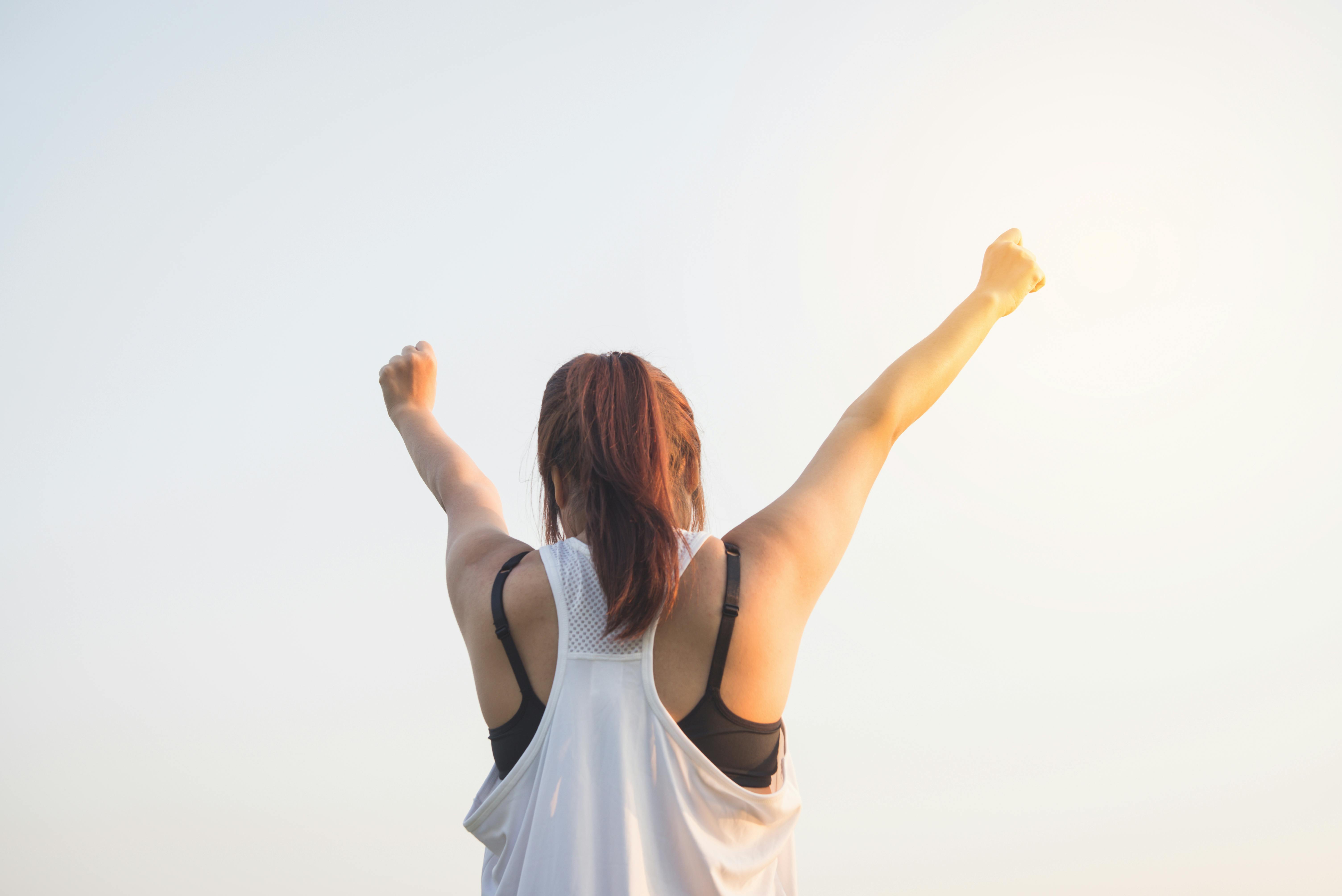 Person celebrating with arms raised against a bright background.